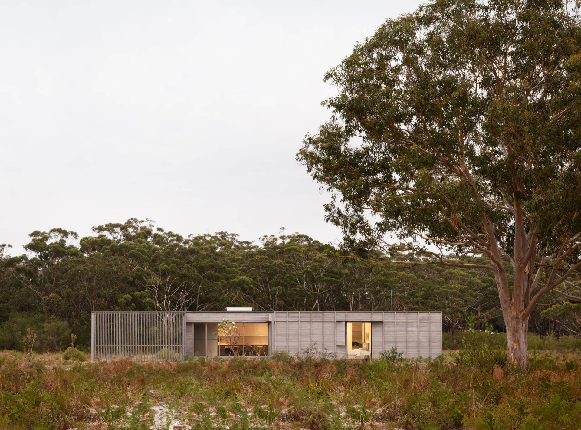 The home’s form is simple and familiar, yet subtly redefined. A generously scaled verandah anchors the dwelling and extends its living space outward, functioning more like an outdoor room than a traditional porch. This shaded threshold becomes a true living zone, equally suited to quiet mornings or social evenings, and acts as a natural bridge between the home’s interior and the landscape beyond.