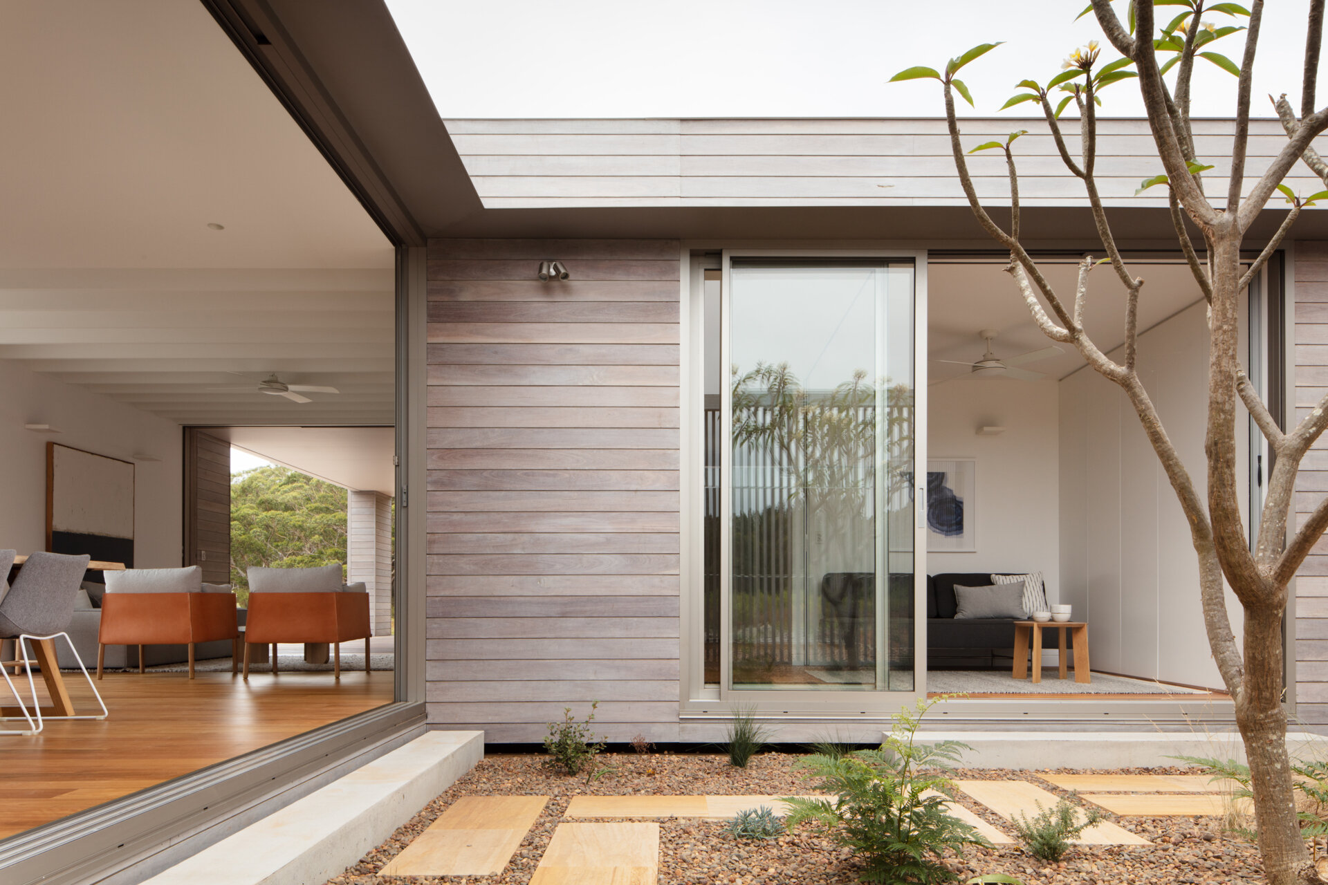 The transition from exterior to interior is just a step. Inside, the living room strikes a perfect balance between cozy and contemporary. The palette leans warm and natural, anchored by rich timber flooring that adds depth and warmth underfoot.