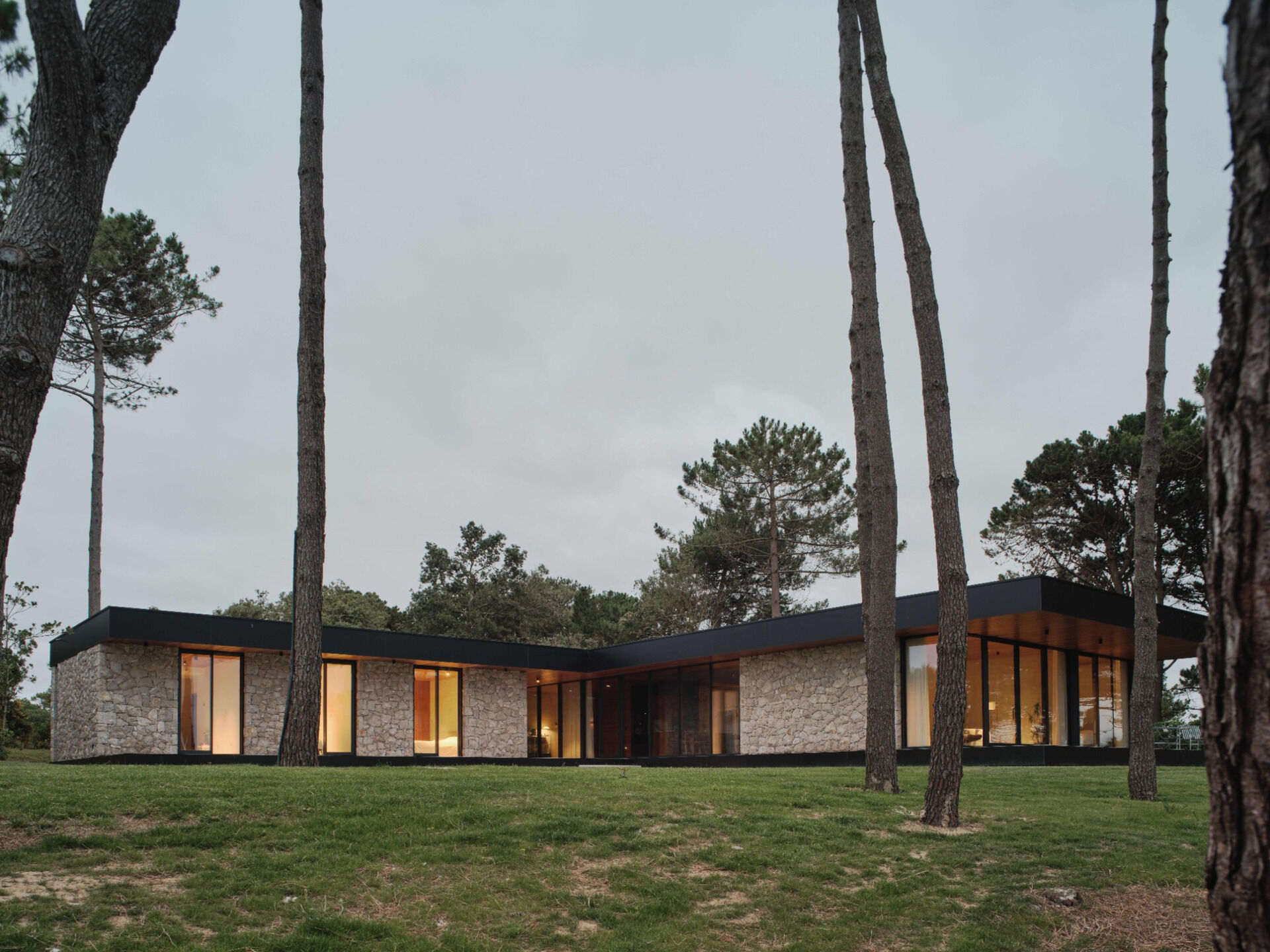 This modern home has stone walls and large glass panels that form a rhythm of solid and void, while slatted wood ceilings, inside and out, accentuate the directional flow toward the sea.
