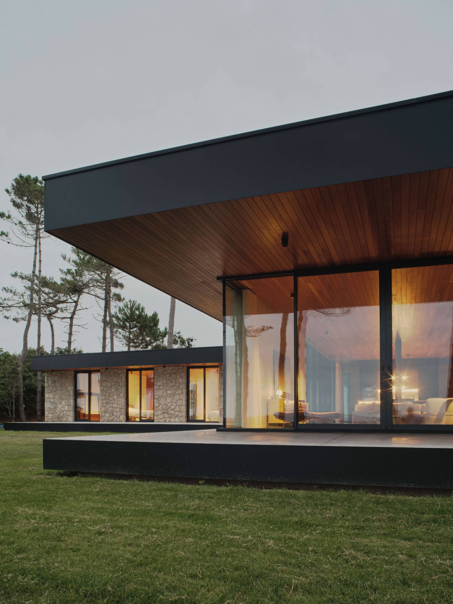 This modern home has large glass panels that form a rhythm of solid and void, while slatted wood ceilings, inside and out, accentuate the directional flow toward the sea.