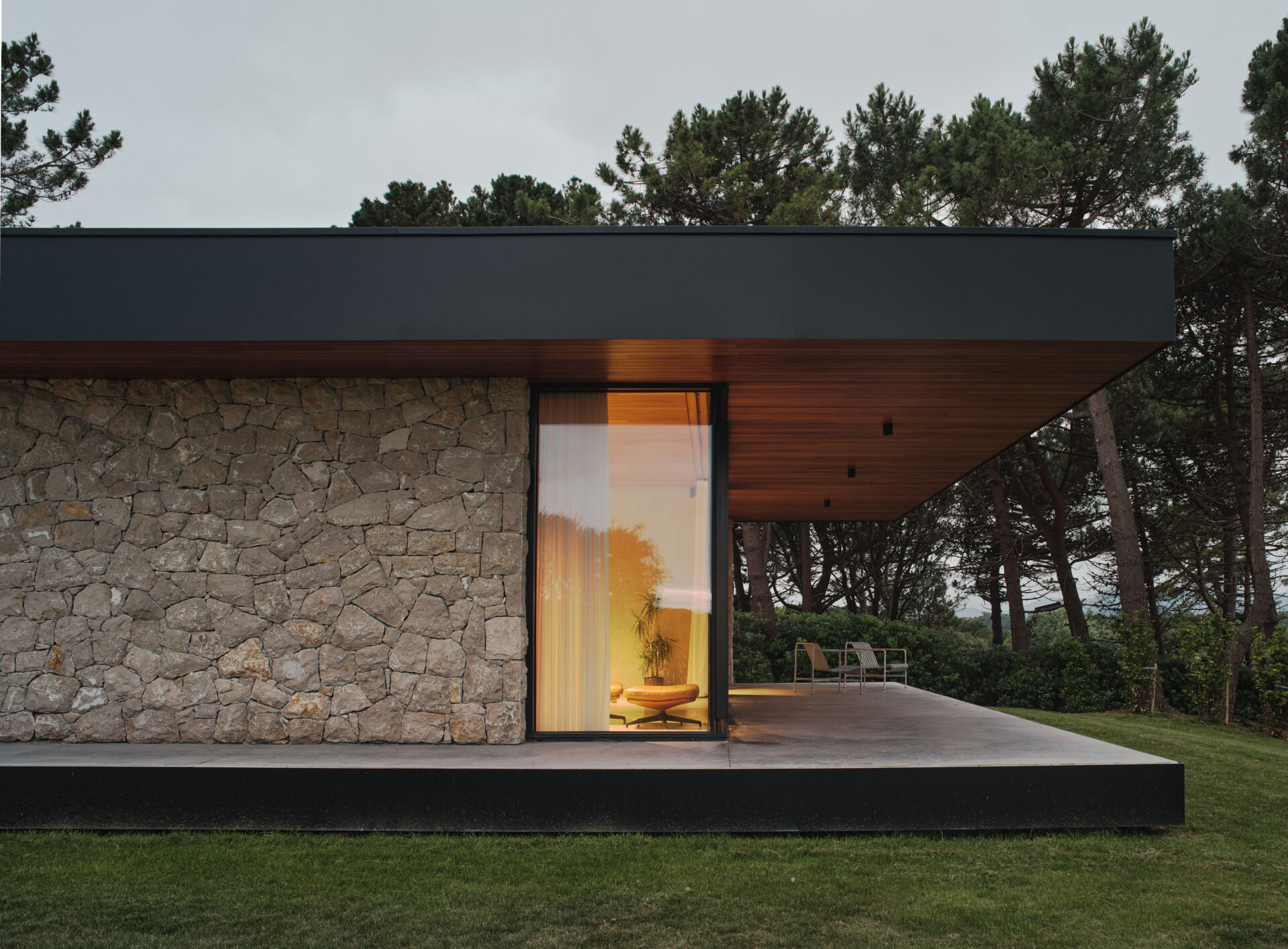 A cast-in-place concrete deck wraps around the home, slightly elevated from the lawn to create a seamless extension of the interior living space. Its smooth surface edge reflect the home's minimalist language while providing a durable platform for enjoying the surrounding landscape.