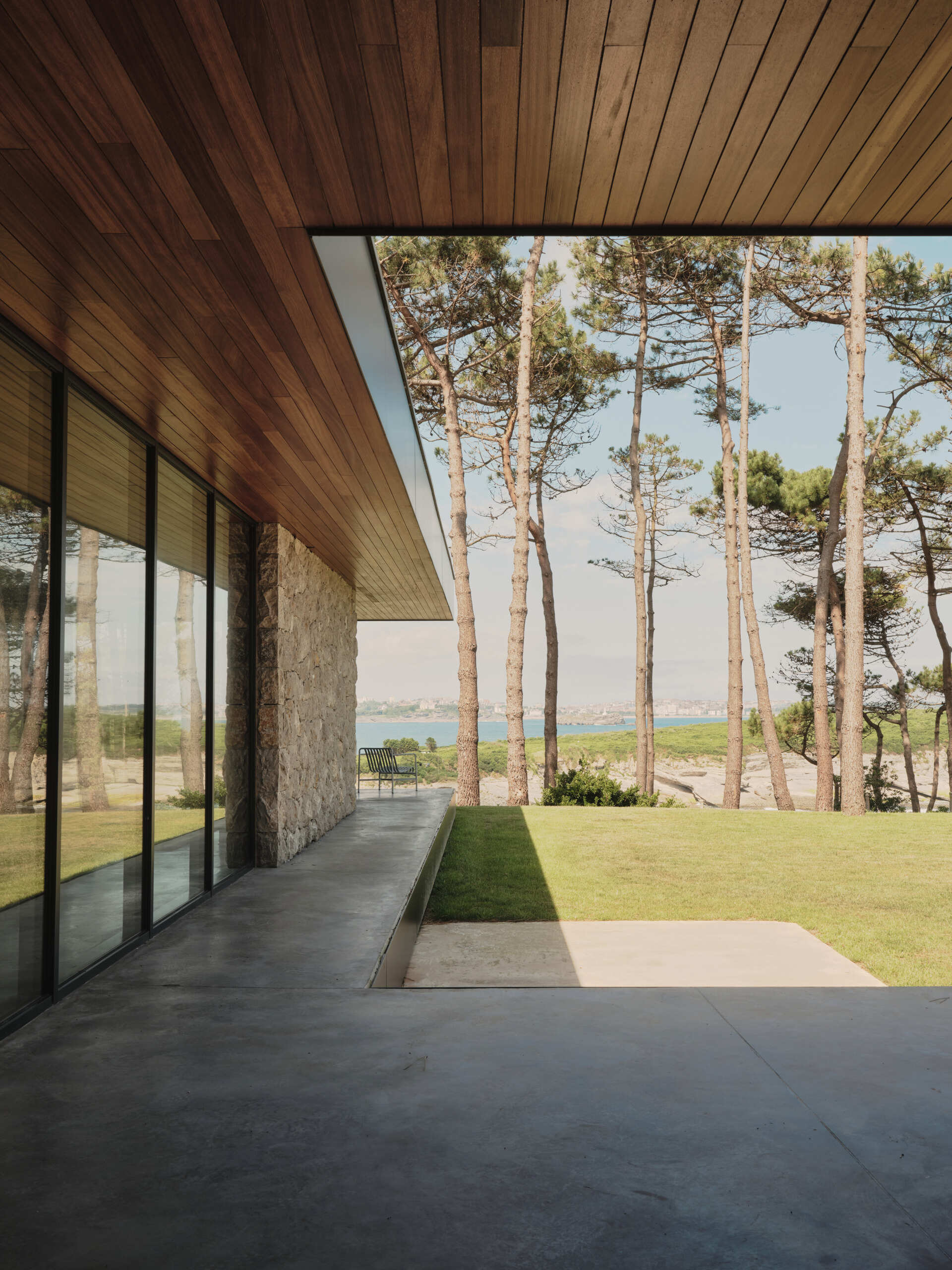 A cast-in-place concrete deck wraps around the home, slightly elevated from the lawn to create a seamless extension of the interior living space. Its smooth surface edge reflect the home's minimalist language while providing a durable platform for enjoying the surrounding landscape.
