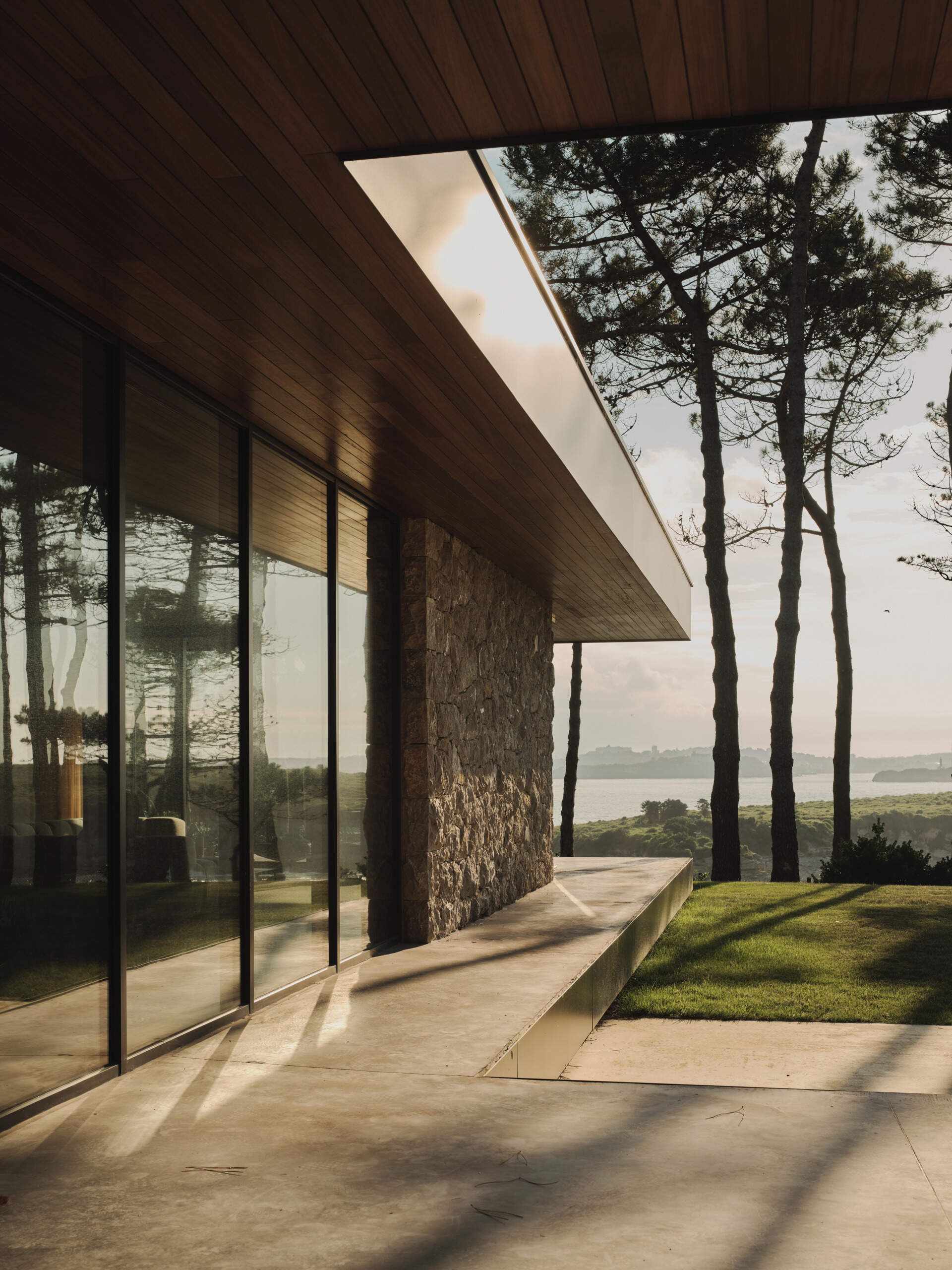 A cast-in-place concrete deck wraps around the home, slightly elevated from the lawn to create a seamless extension of the interior living space. Its smooth surface edge reflect the home's minimalist language while providing a durable platform for enjoying the surrounding landscape.