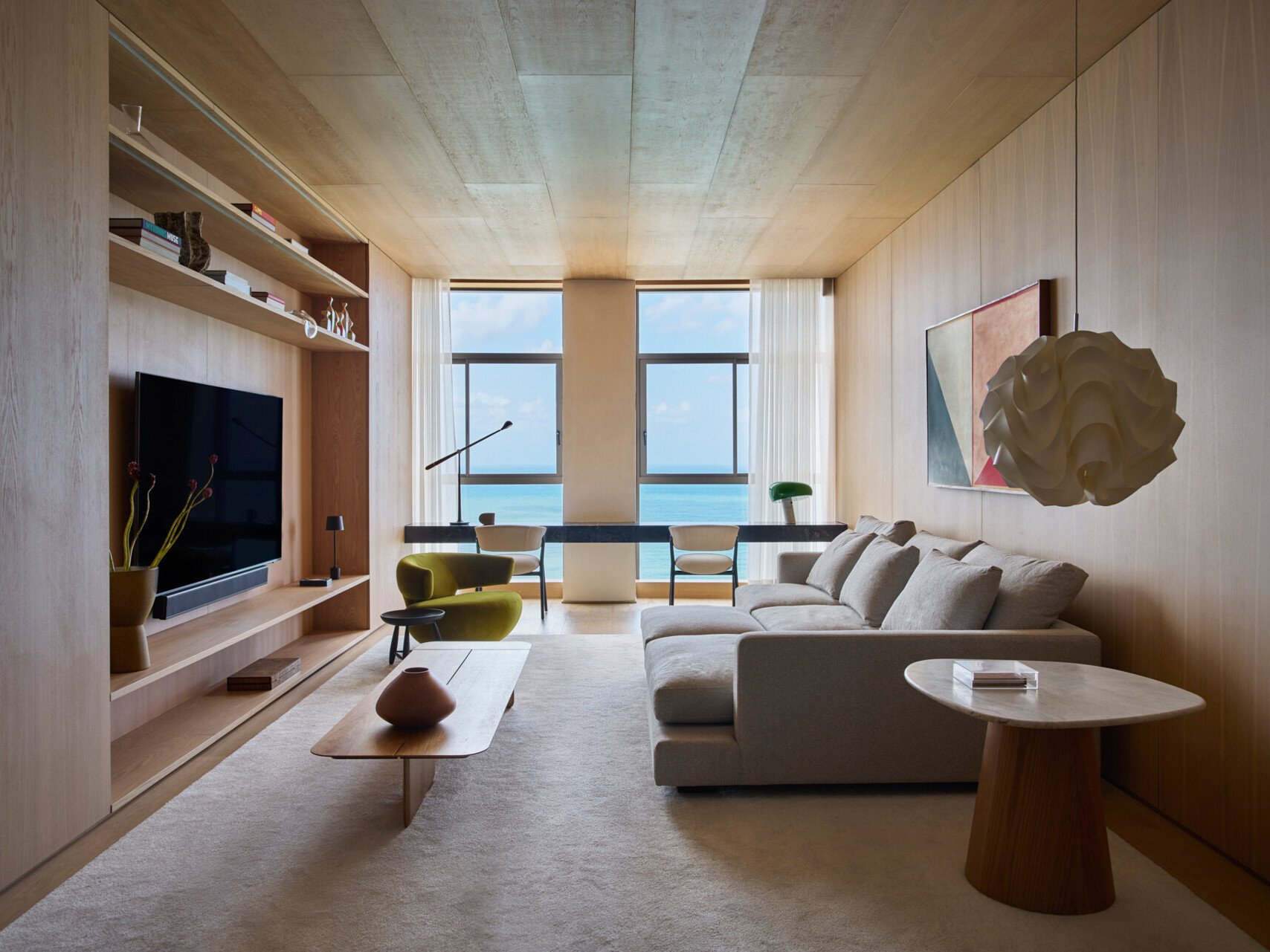 This modern TV room is located on the lower floor, along with the bedrooms and bathrooms. Natural wood cabinetry brings warmth to the TV room, supporting the calm atmosphere of the private level, while a desk runs along the wall facing out towards the views.