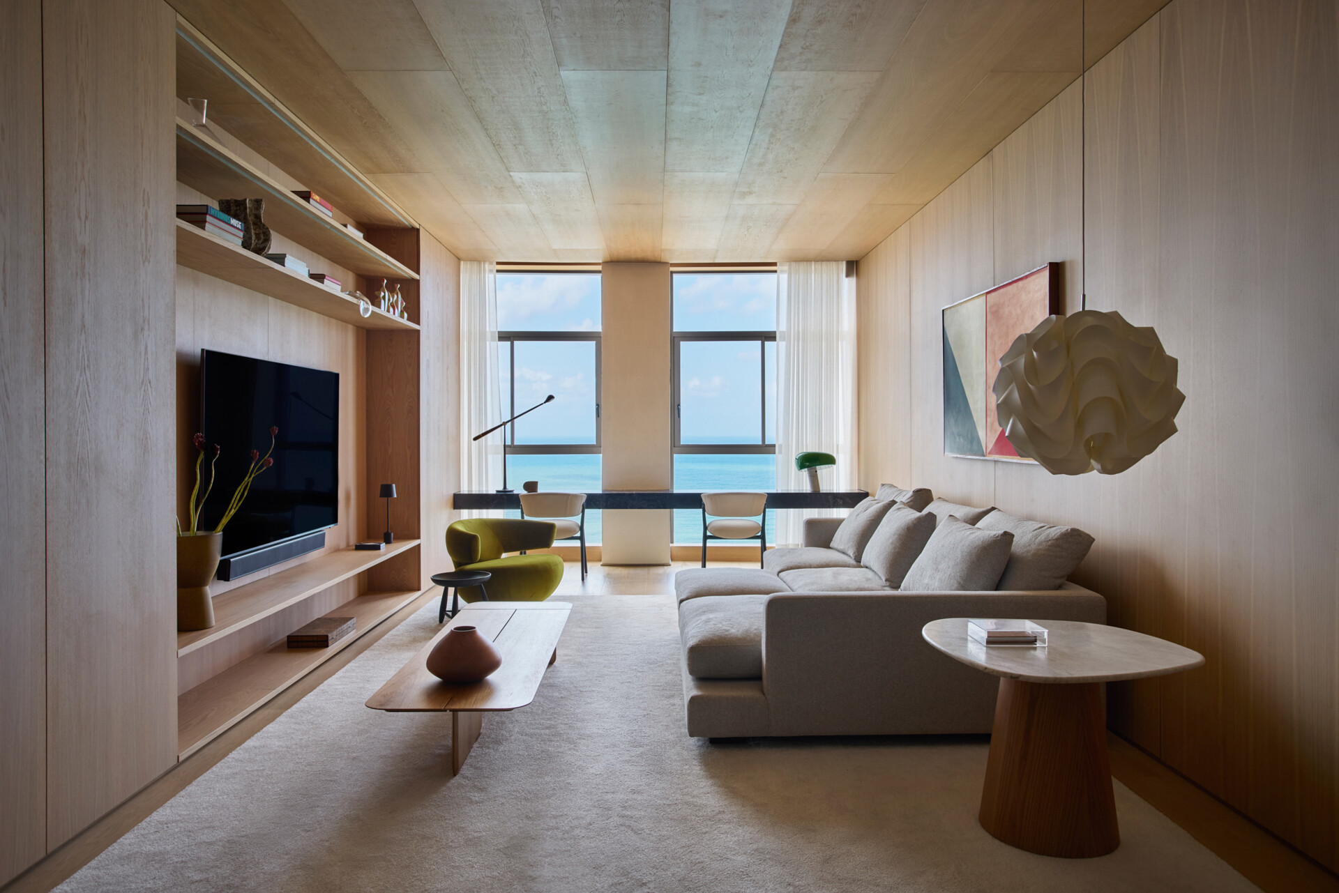 This modern TV room is located on the lower floor, along with the bedrooms and bathrooms. Natural wood cabinetry brings warmth to the TV room, supporting the calm atmosphere of the private level, while a desk runs along the wall facing out towards the views.