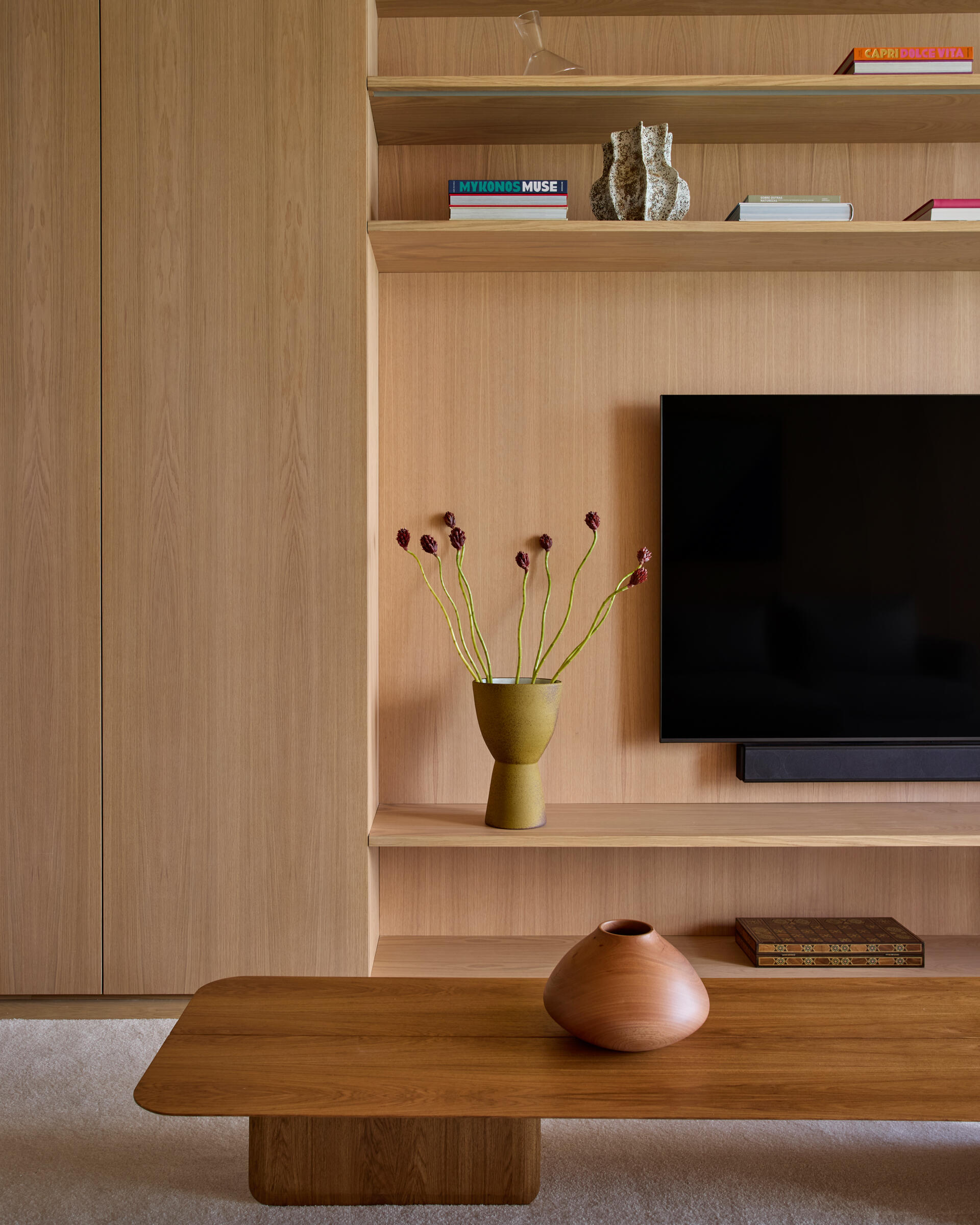 This modern TV room is located on the lower floor, along with the bedrooms and bathrooms. Natural wood cabinetry brings warmth to the TV room, supporting the calm atmosphere of the private level, while a desk runs along the wall facing out towards the views.