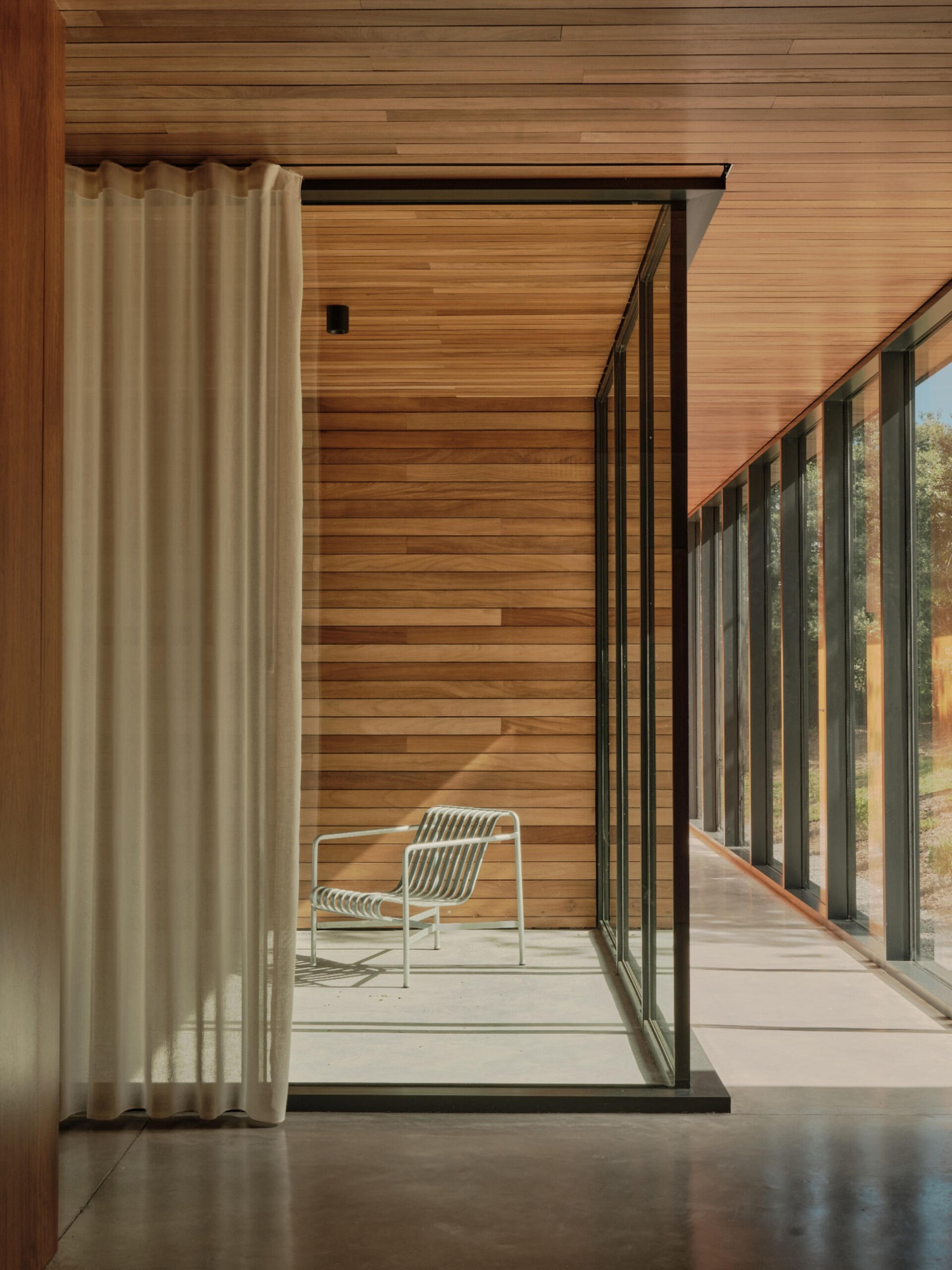 A modern home interior that features wood ceiling and walls, concrete flooring, and walls of glass.