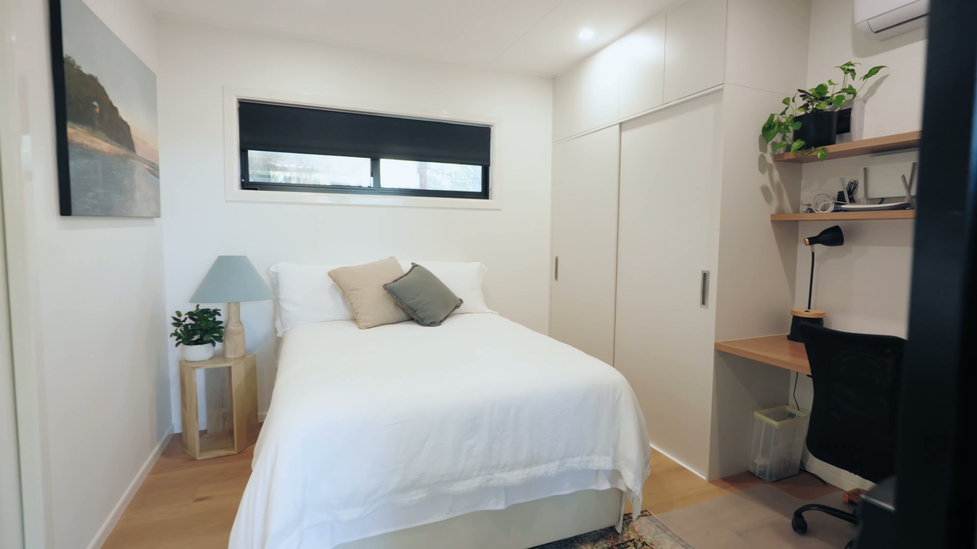 A quiet, efficient bedroom in a container home has with a full-height wardrobe with overhead storage, and a built-in desk designed for working from home in comfort.