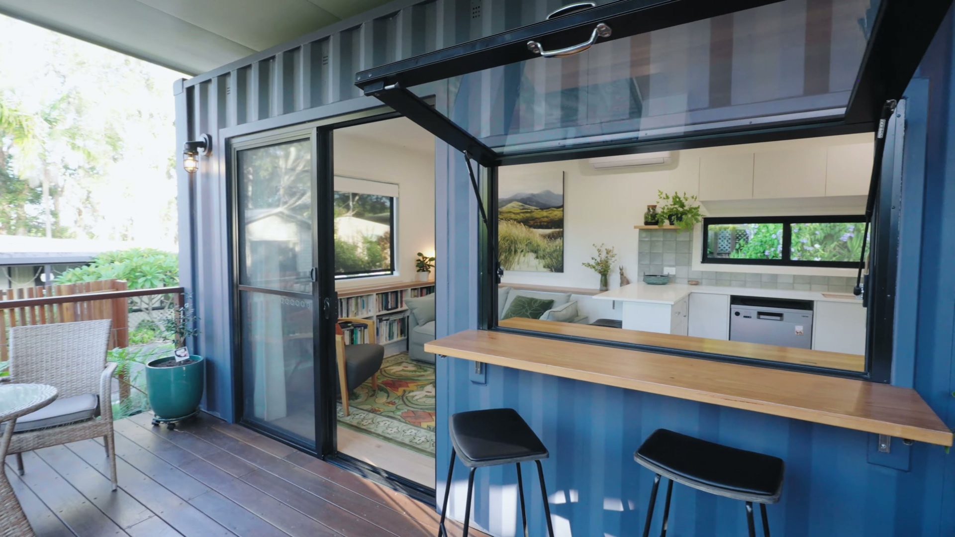 A private rear deck framed by two container units, designed for seamless indoor-outdoor living with natural shade and a relaxed coastal feel.