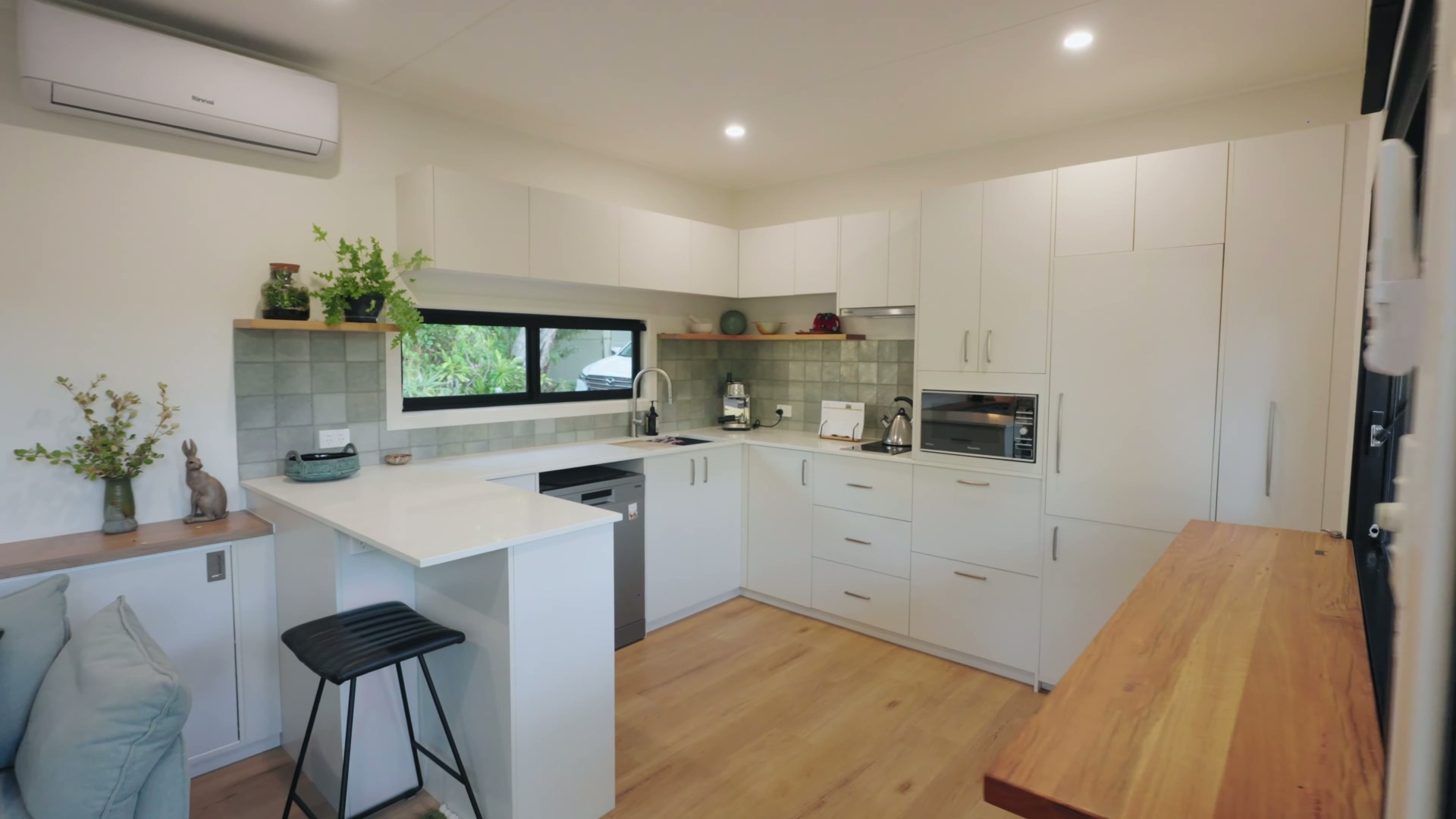 A custom kitchen with white cabinets, soft green tiles, and accents, features space-saving joinery, a slimline induction cooktop, and handcrafted tile details.