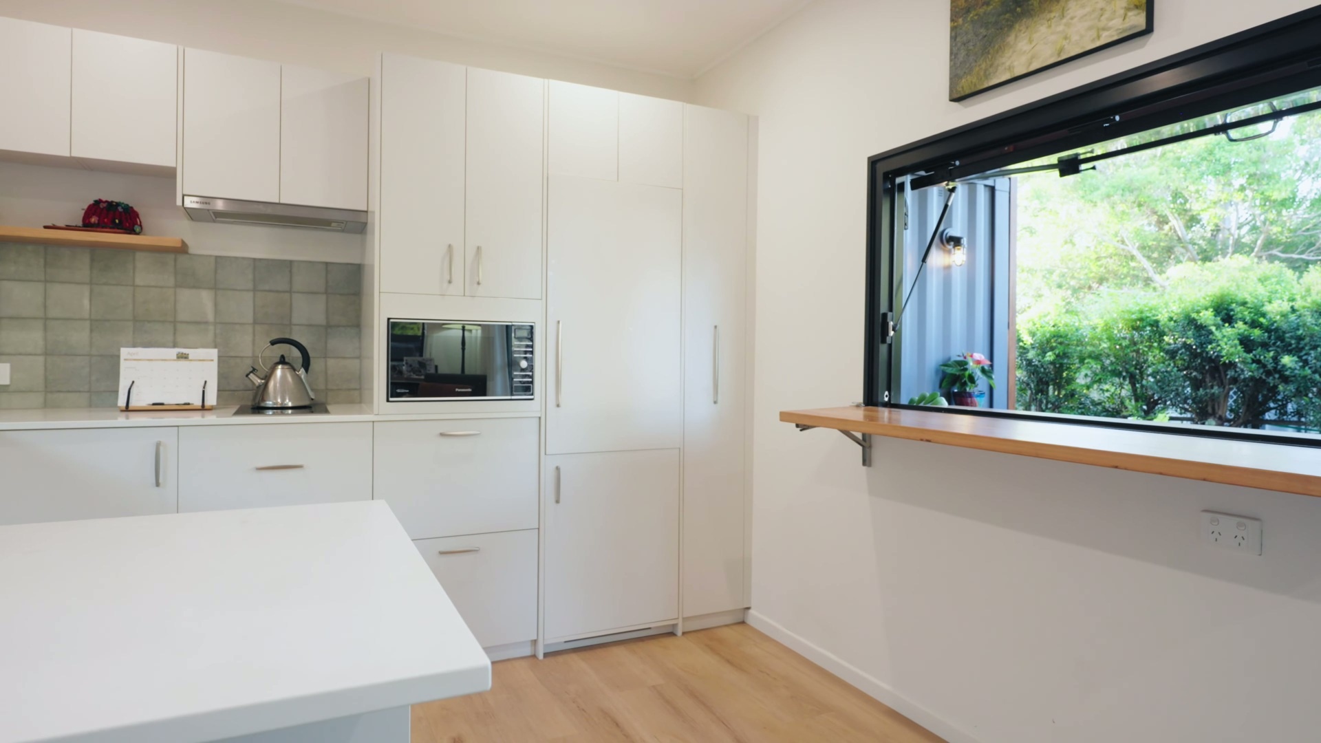 A custom kitchen with white cabinets, soft green tiles, and accents, features space-saving joinery, a slimline induction cooktop, and handcrafted tile details.