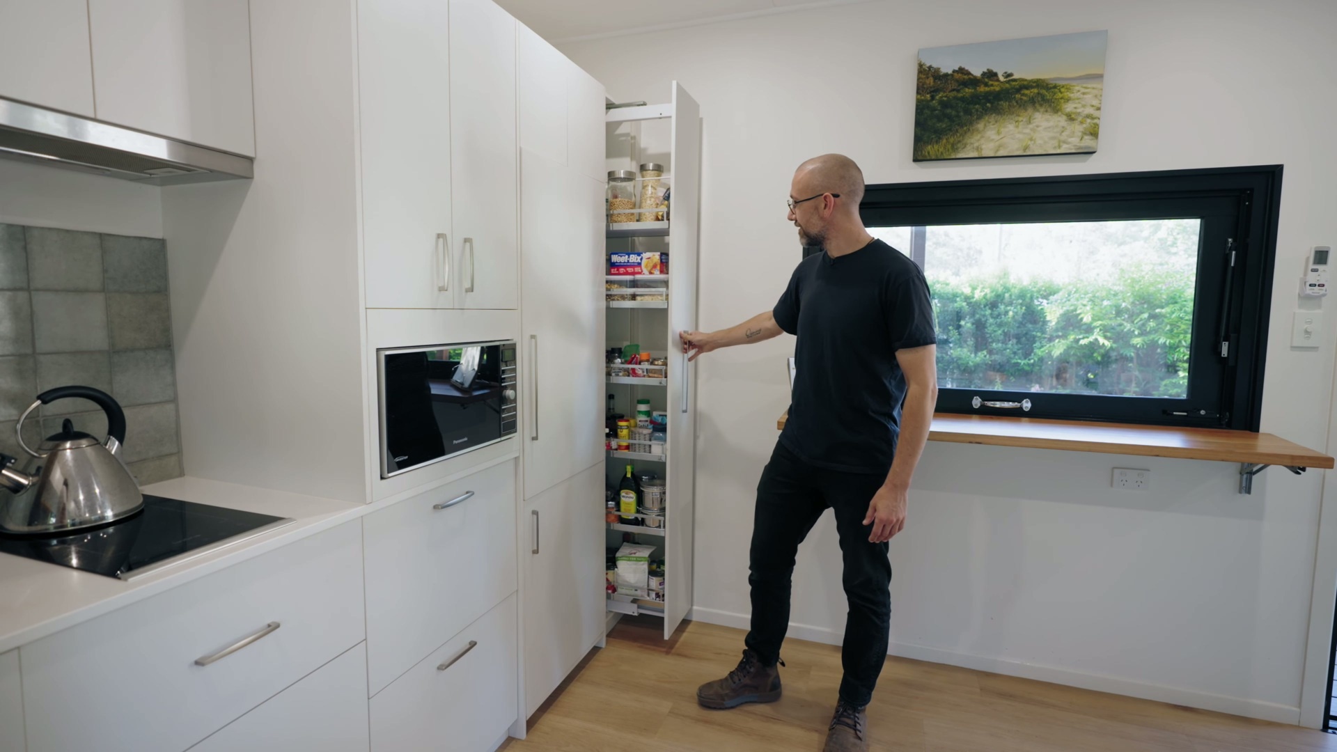 A custom kitchen with white cabinets, soft green tiles, and accents, features space-saving joinery, a slimline induction cooktop, and handcrafted tile details.