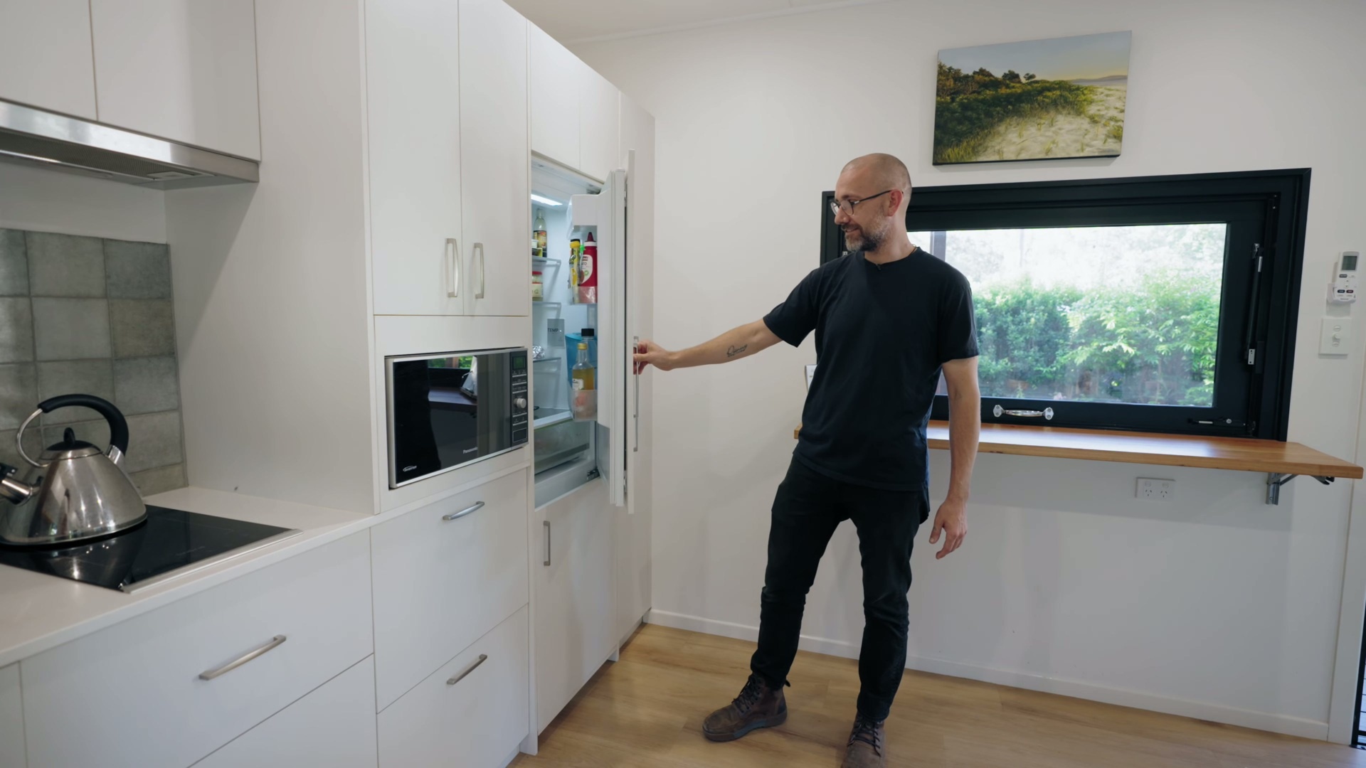 A custom kitchen with white cabinets, soft green tiles, and accents, features space-saving joinery, a slimline induction cooktop, and handcrafted tile details.