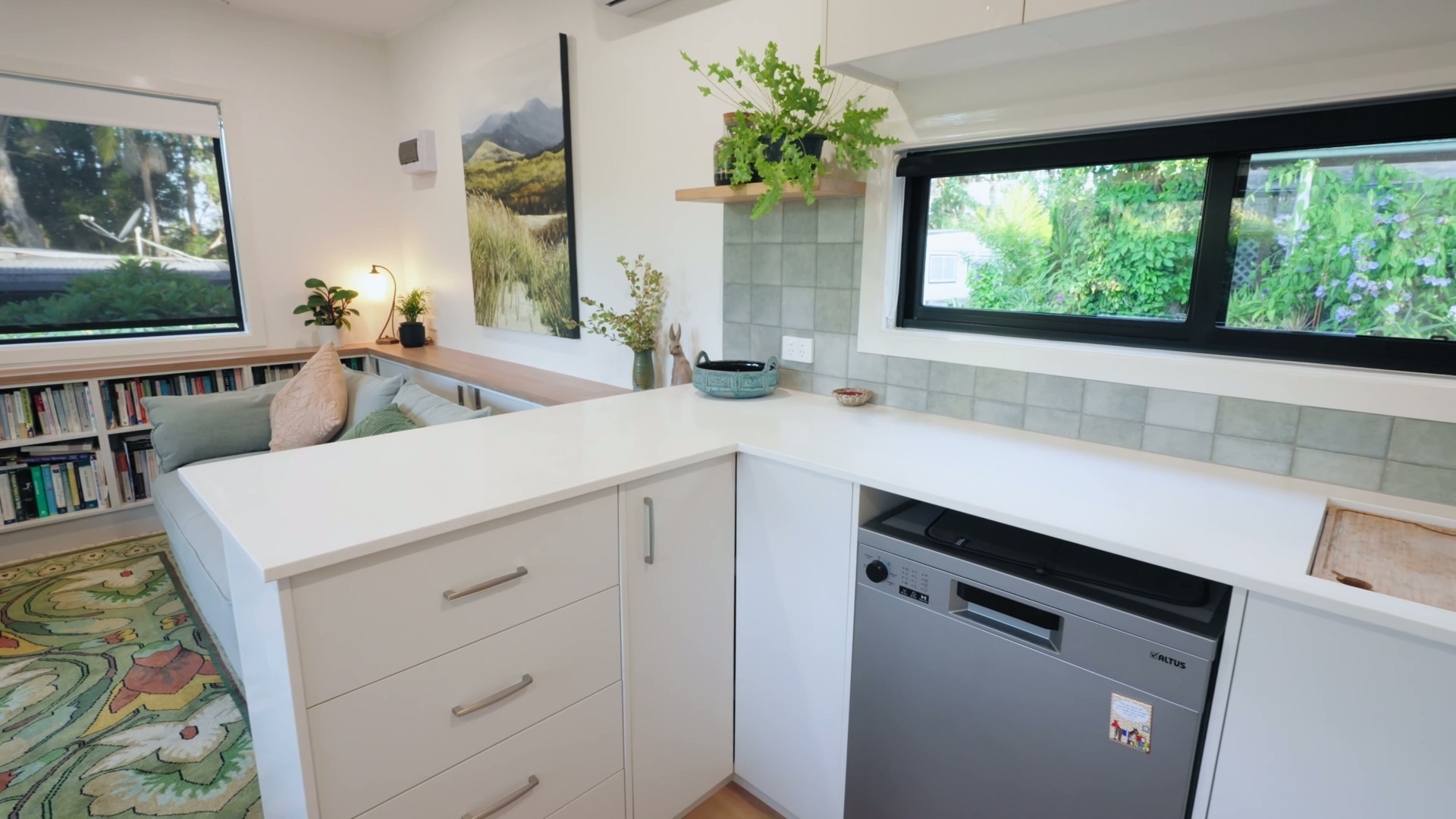 A custom kitchen with white cabinets, soft green tiles, and accents, features space-saving joinery, a slimline induction cooktop, and handcrafted tile details.