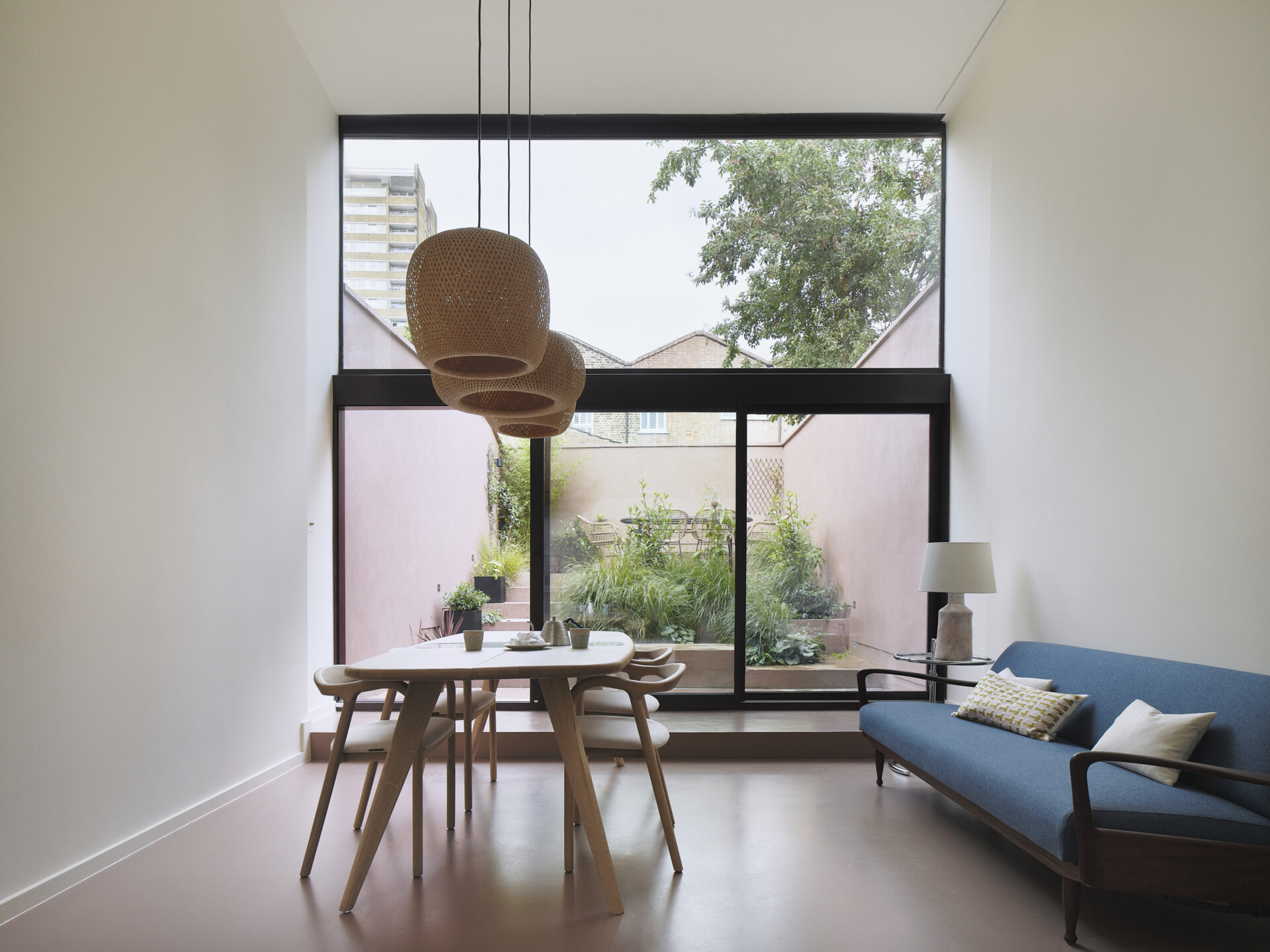 Inside this home with double-height windows, there's an open-plan living and dining space. Rather than falling into the trap of a typical basement conversion, the designers opened up the lower ground floor entirely. This ambitious extension now connects seamlessly to the garden through a stepped surface that mimics a natural slope. Overhead, a dramatic roofscape of skylights mirrors the ground’s topography, ushering in daylight and elevating the everyday into spectacle.