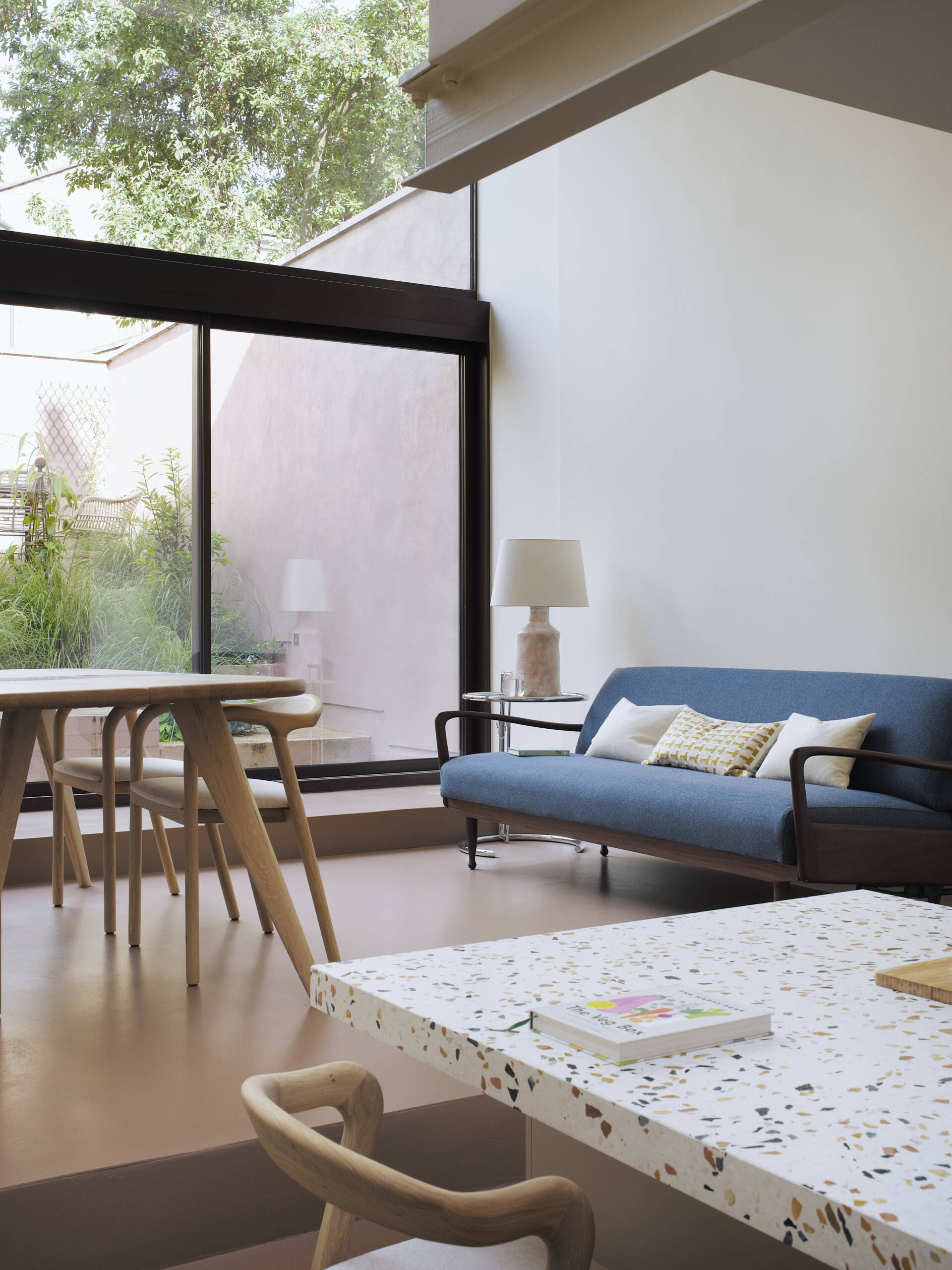 Inside this home with double-height windows, there's an open-plan living and dining space. Rather than falling into the trap of a typical basement conversion, the designers opened up the lower ground floor entirely. This ambitious extension now connects seamlessly to the garden through a stepped surface that mimics a natural slope. Overhead, a dramatic roofscape of skylights mirrors the ground’s topography, ushering in daylight and elevating the everyday into spectacle.