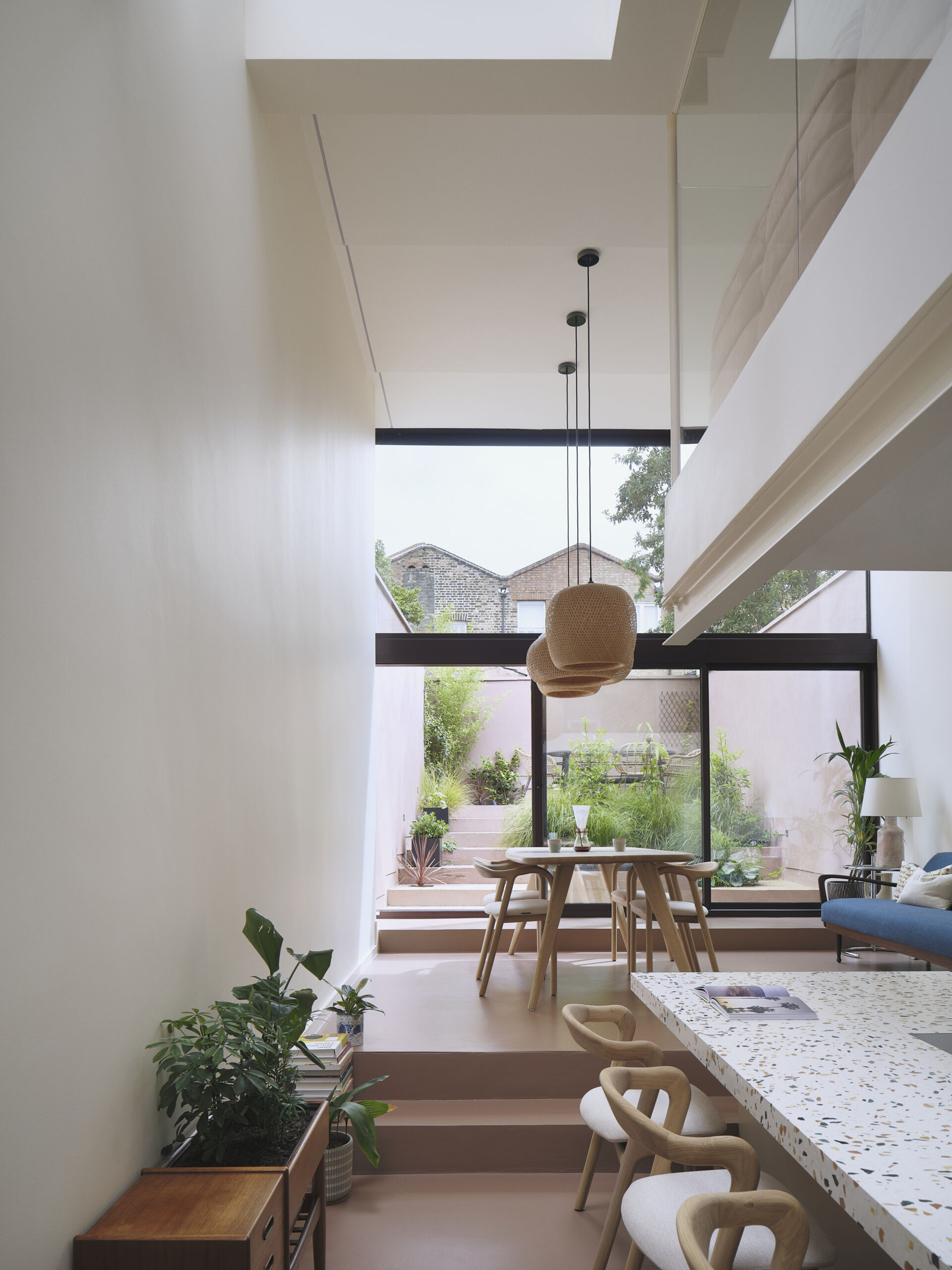 Inside this home with double-height windows, there's an open-plan living and dining space. Rather than falling into the trap of a typical basement conversion, the designers opened up the lower ground floor entirely. This ambitious extension now connects seamlessly to the garden through a stepped surface that mimics a natural slope. Overhead, a dramatic roofscape of skylights mirrors the ground’s topography, ushering in daylight and elevating the everyday into spectacle.