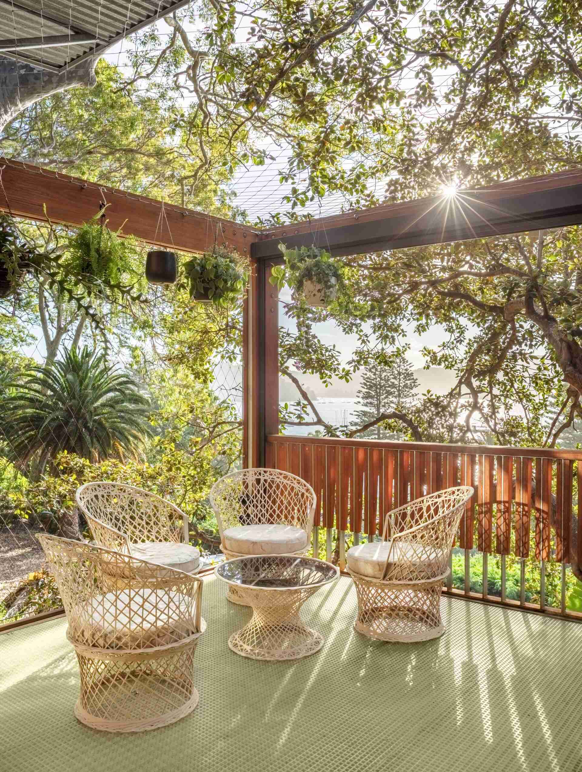 In this outdoor seating area, simple wicker chairs and a small table set the tone in this relaxed corner of the deck. Surrounded by plants and filtered sunlight, it’s the kind of space that doesn’t need much to feel complete.