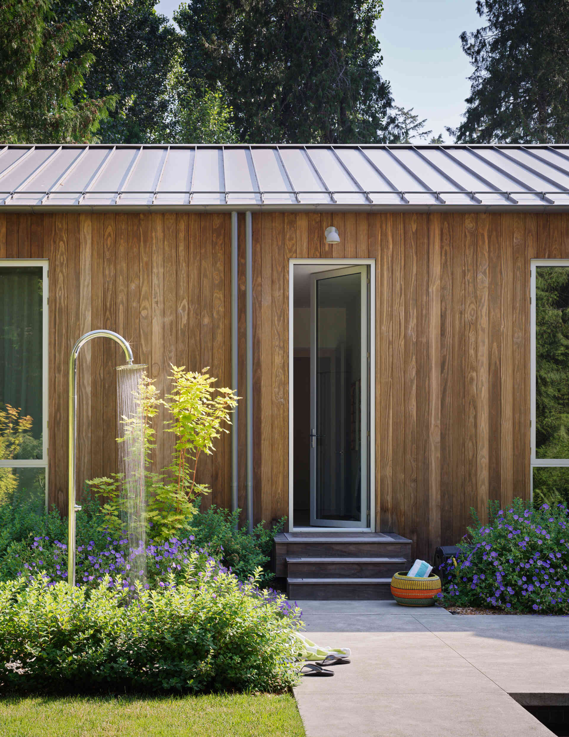 Outdoor life at this modern home is central to the family's daily rhythm. A generous lawn stretches out from the home, giving space for play and relaxation. At its far edge, a swimming pool and spa sit in full sun, paired with a stone-paved lounging terrace and outdoor shower.