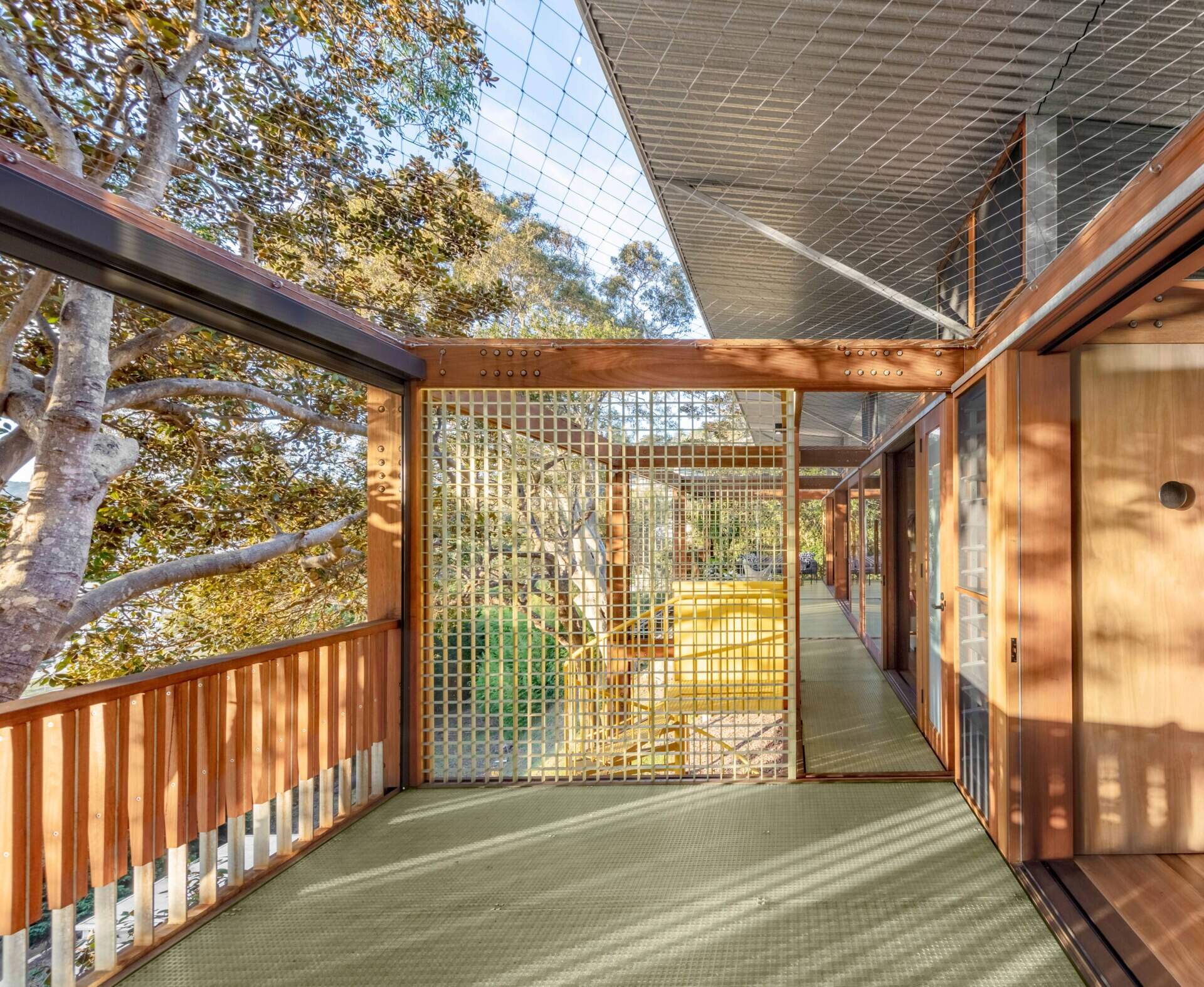 Surrounded by trees and filtered sunshine, the open outdoor corridor feels like part garden path, part gallery, connecting spaces with calm and a quiet rhythm of its own.
