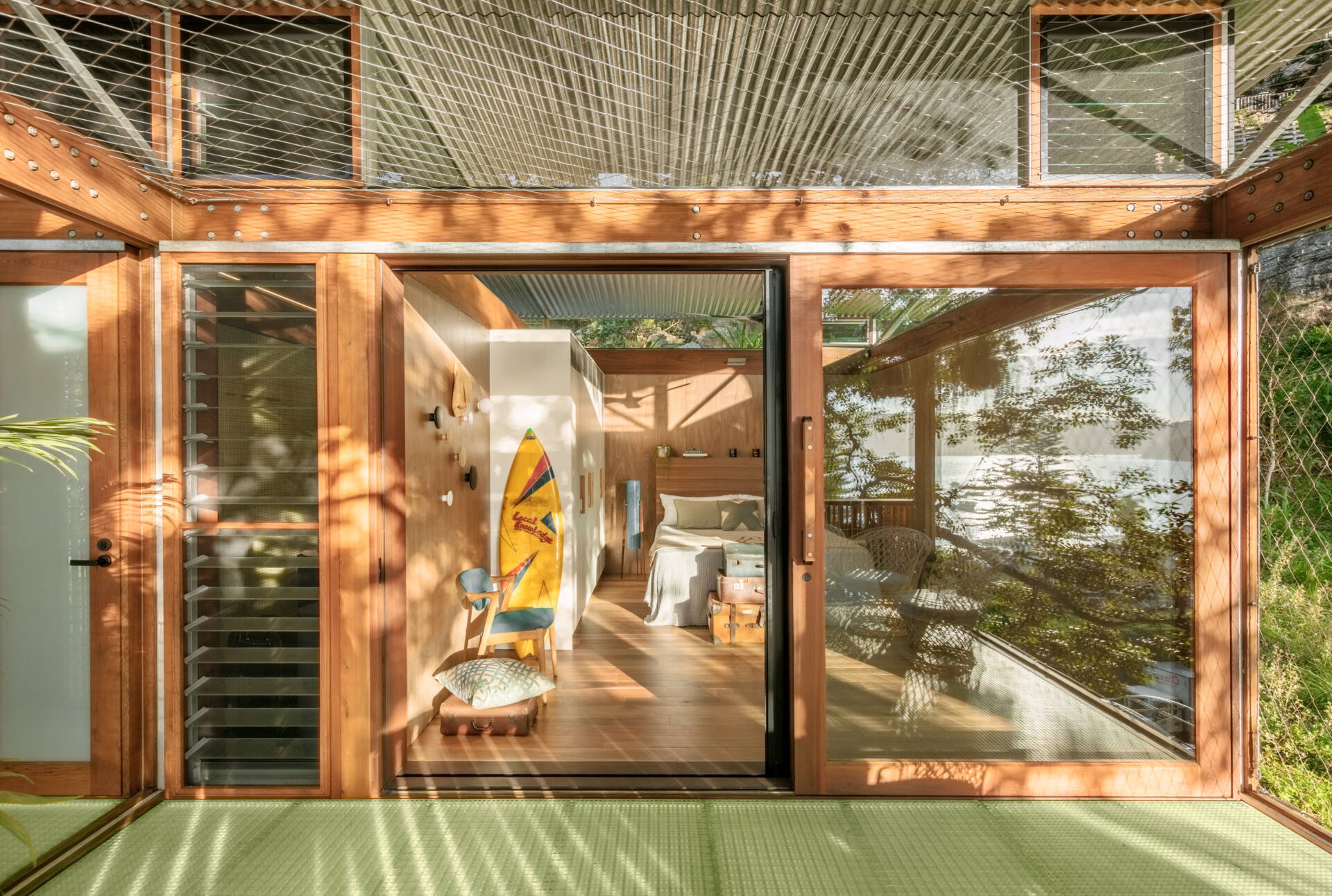 Lined in warm timber and open to the light, the main bedroom keeps things simple. A sliding wood-framed glass door opens the room, while vintage suitcases by the bed add a gentle lived-in feel.