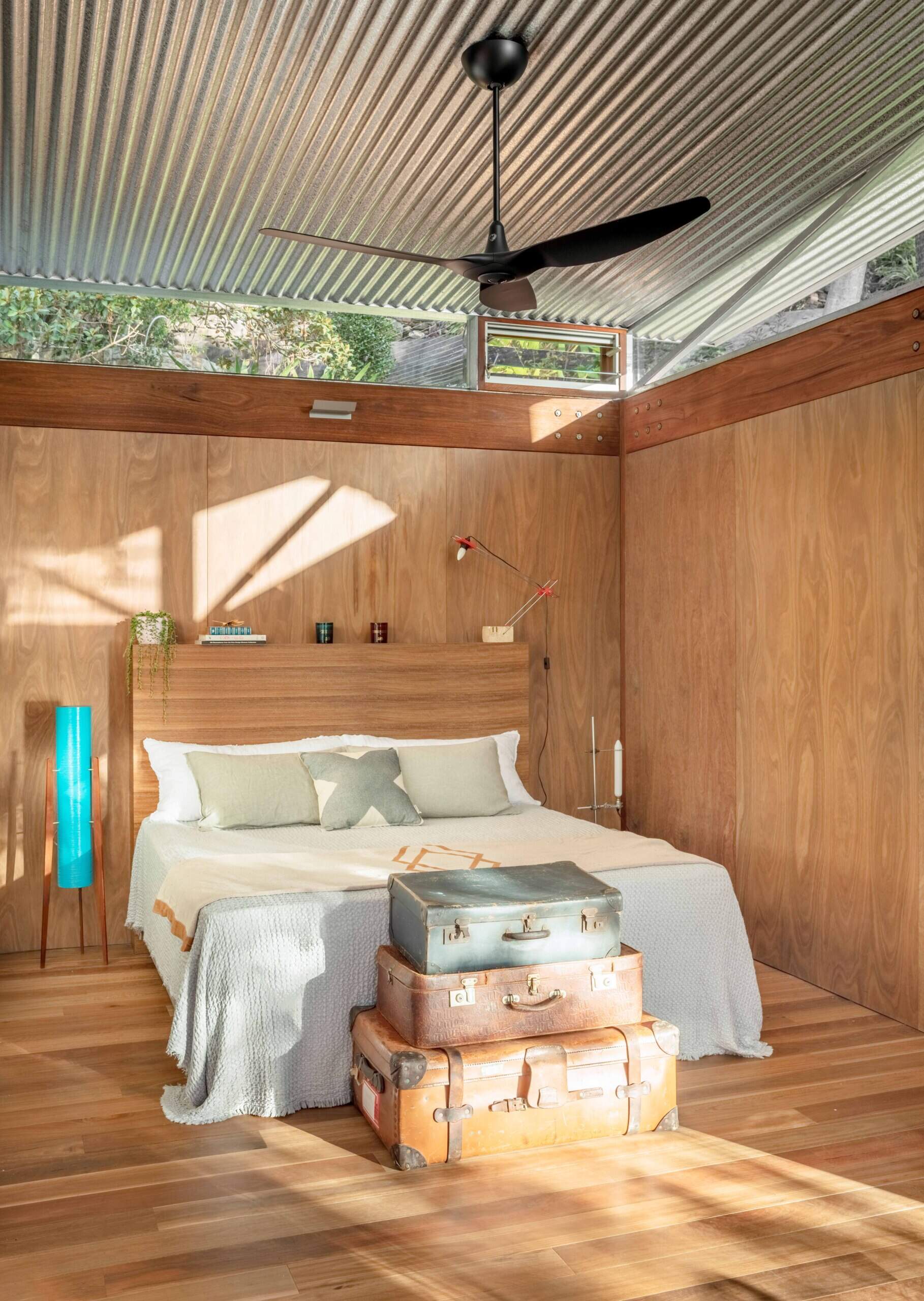 Lined in warm timber and open to the light, the main bedroom keeps things simple. A sliding wood-framed glass door opens the room, while vintage suitcases by the bed add a gentle lived-in feel.