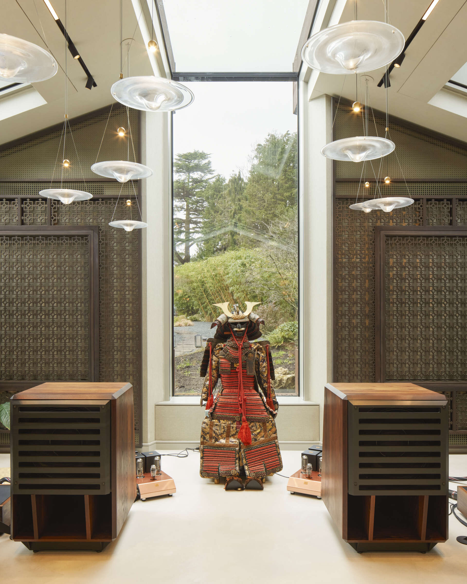 The interior of this modern music pavilion is a refined blend of sound-focused design and artful display, featuring custom joinery, soft lighting, and a cascading glass pendant that reflects like ripples across the minimalist micro cement floor.