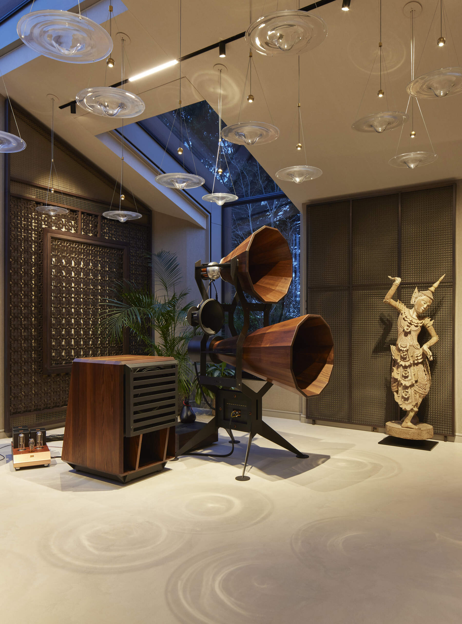 The interior of this modern music pavilion is a refined blend of sound-focused design and artful display, featuring custom joinery, soft lighting, and a cascading glass pendant that reflects like ripples across the minimalist micro cement floor.