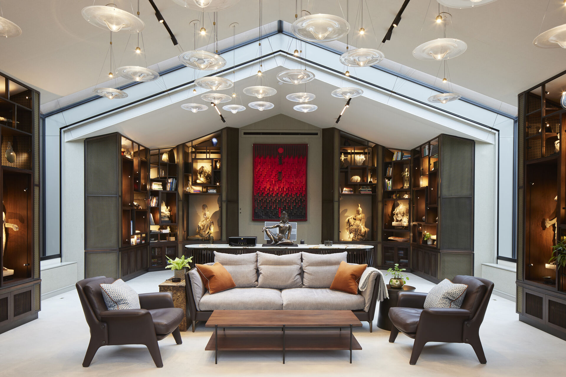 The interior of this modern music pavilion is a refined blend of sound-focused design and artful display, featuring custom joinery, soft lighting, and a cascading glass pendant that reflects like ripples across the minimalist micro cement floor.