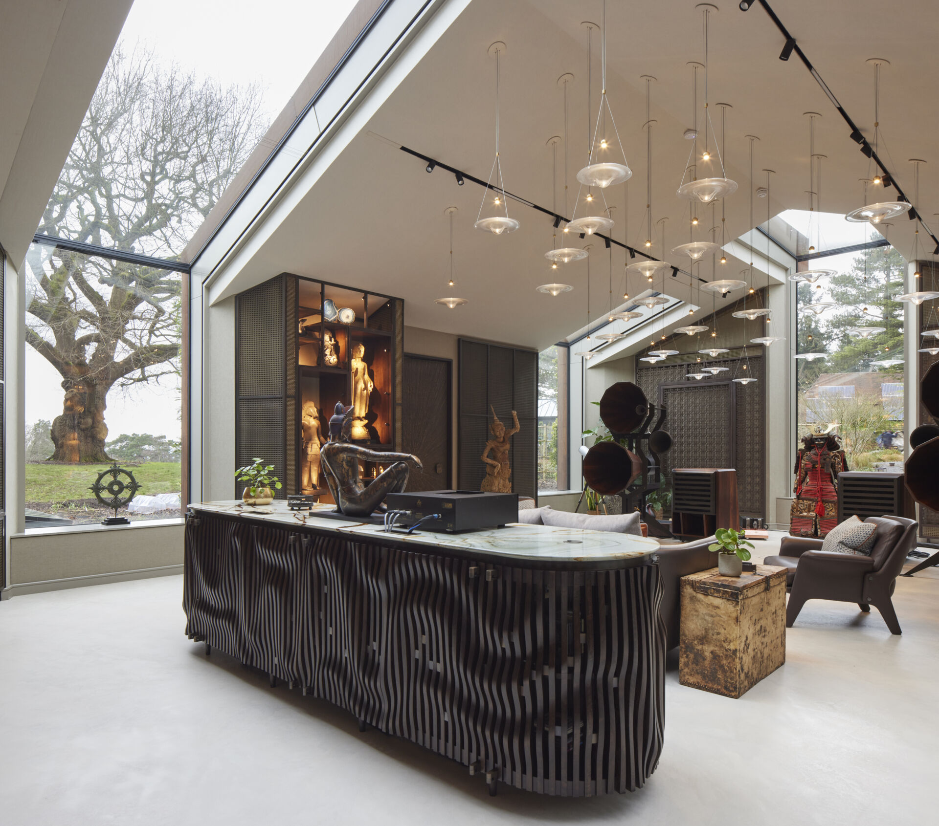 The interior of this modern music pavilion is a refined blend of sound-focused design and artful display, featuring custom joinery, soft lighting, and a cascading glass pendant that reflects like ripples across the minimalist micro cement floor.