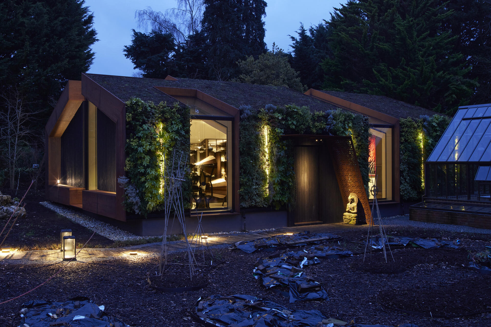 This modern music pavilion blends charred timber, Corten steel, and a living roof to create a sculptural retreat in the landscape. At night, subtle lighting brings the textures to life, softly illuminating its bold architectural form.