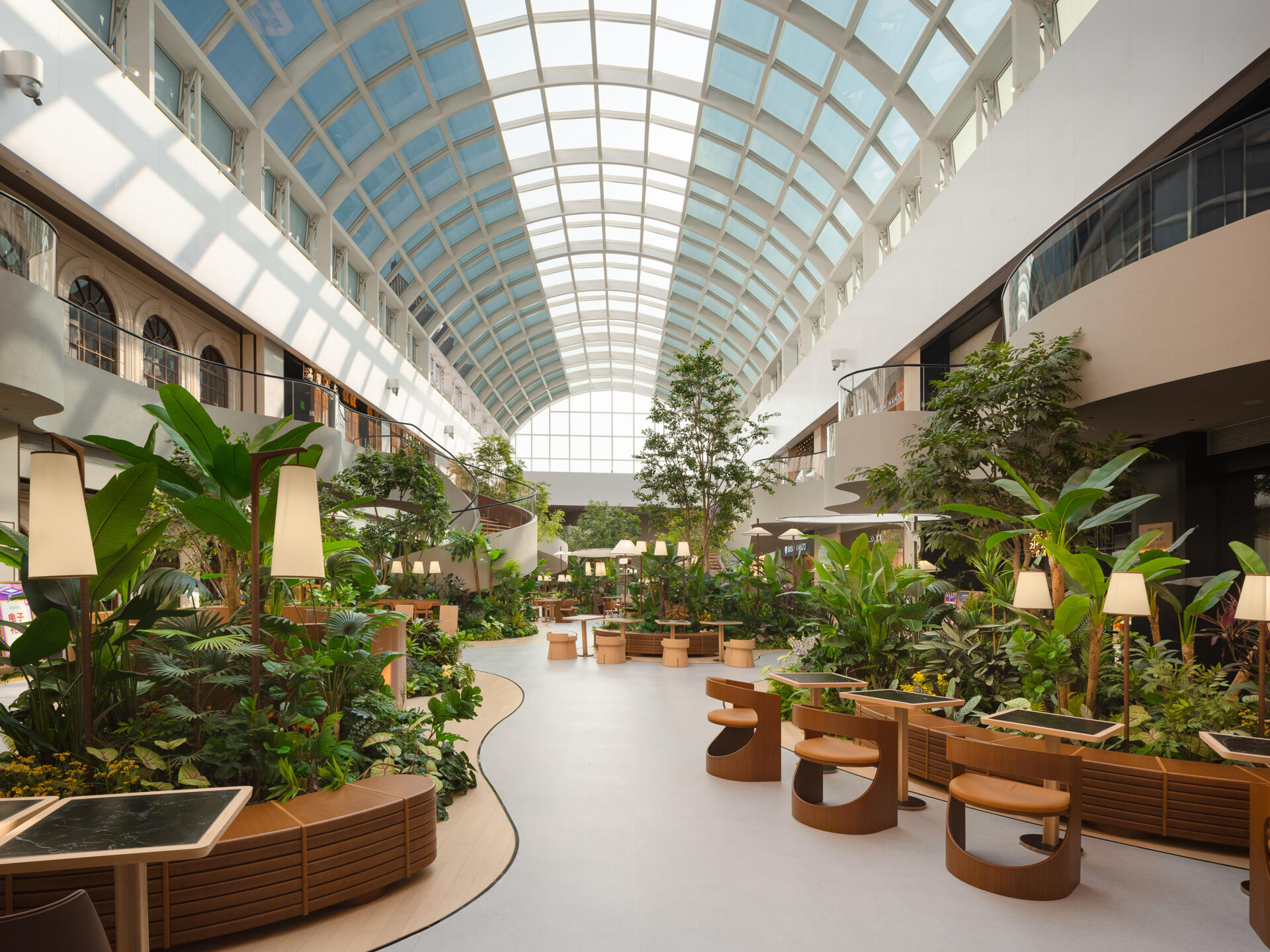 A transparent arched skylight transforms this indoor public garden space with natural light. Steel curves echo leaf veins while shifting sun patterns on the floor mimic moss growing in a greenhouse. A calming, nature-inspired design moment.