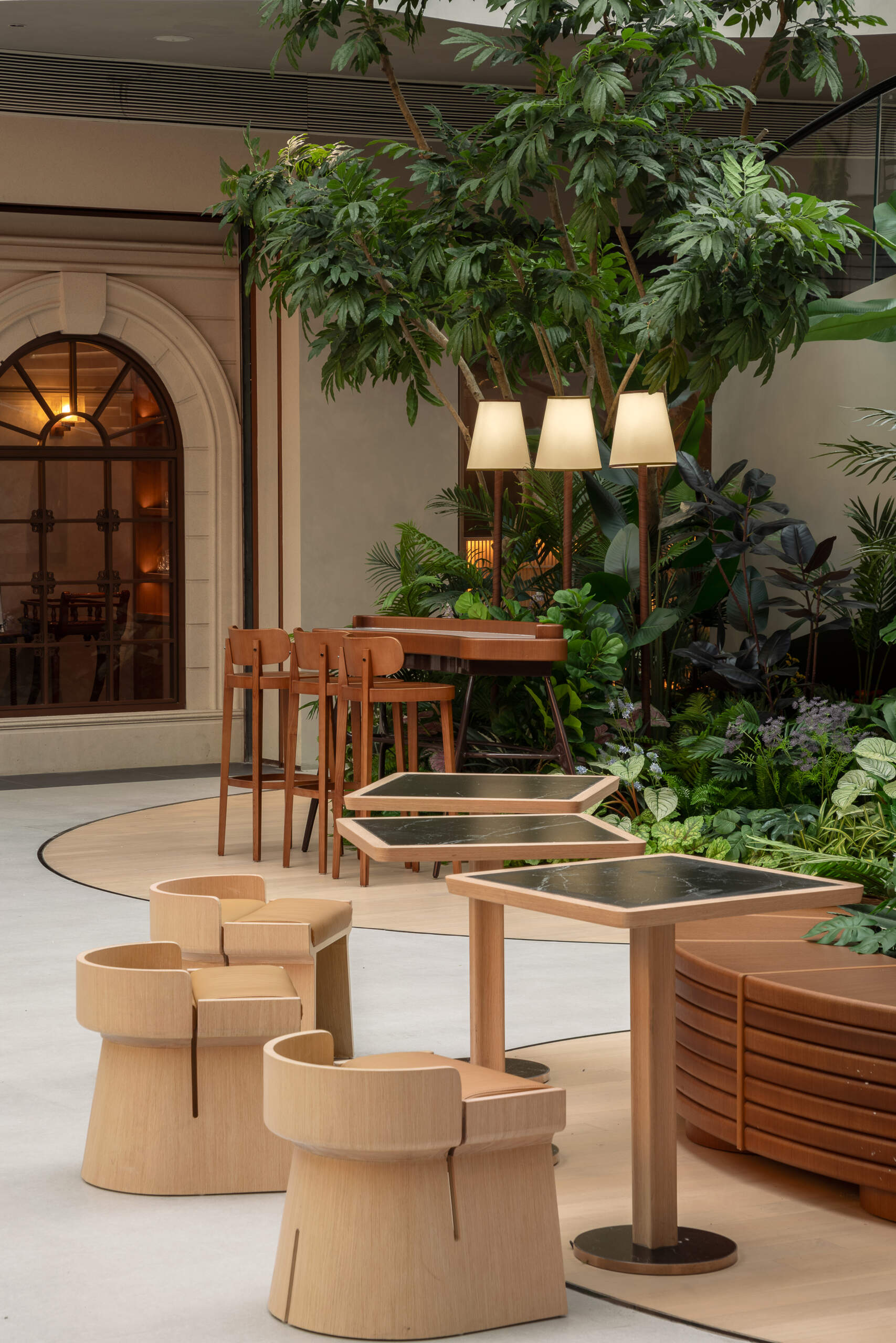 In this public plaza, long benches curve around clusters of greenery while sculptural chairs create relaxed, flexible seating. This dining space flows into a shared public garden, dissolving the line between restaurant and rest stop.