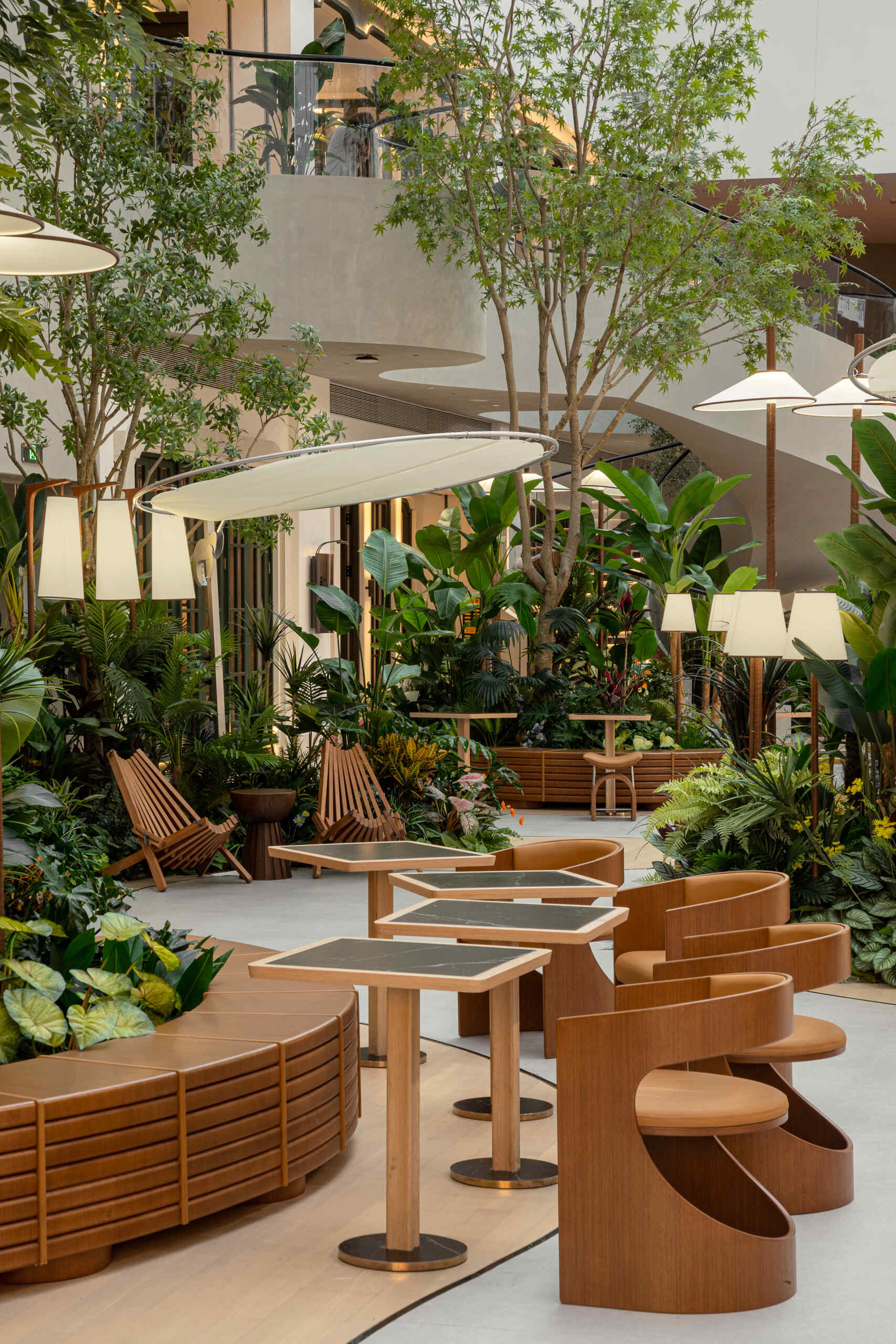 In this public plaza, long benches curve around clusters of greenery while sculptural chairs create relaxed, flexible seating. This dining space flows into a shared public garden, dissolving the line between restaurant and rest stop.