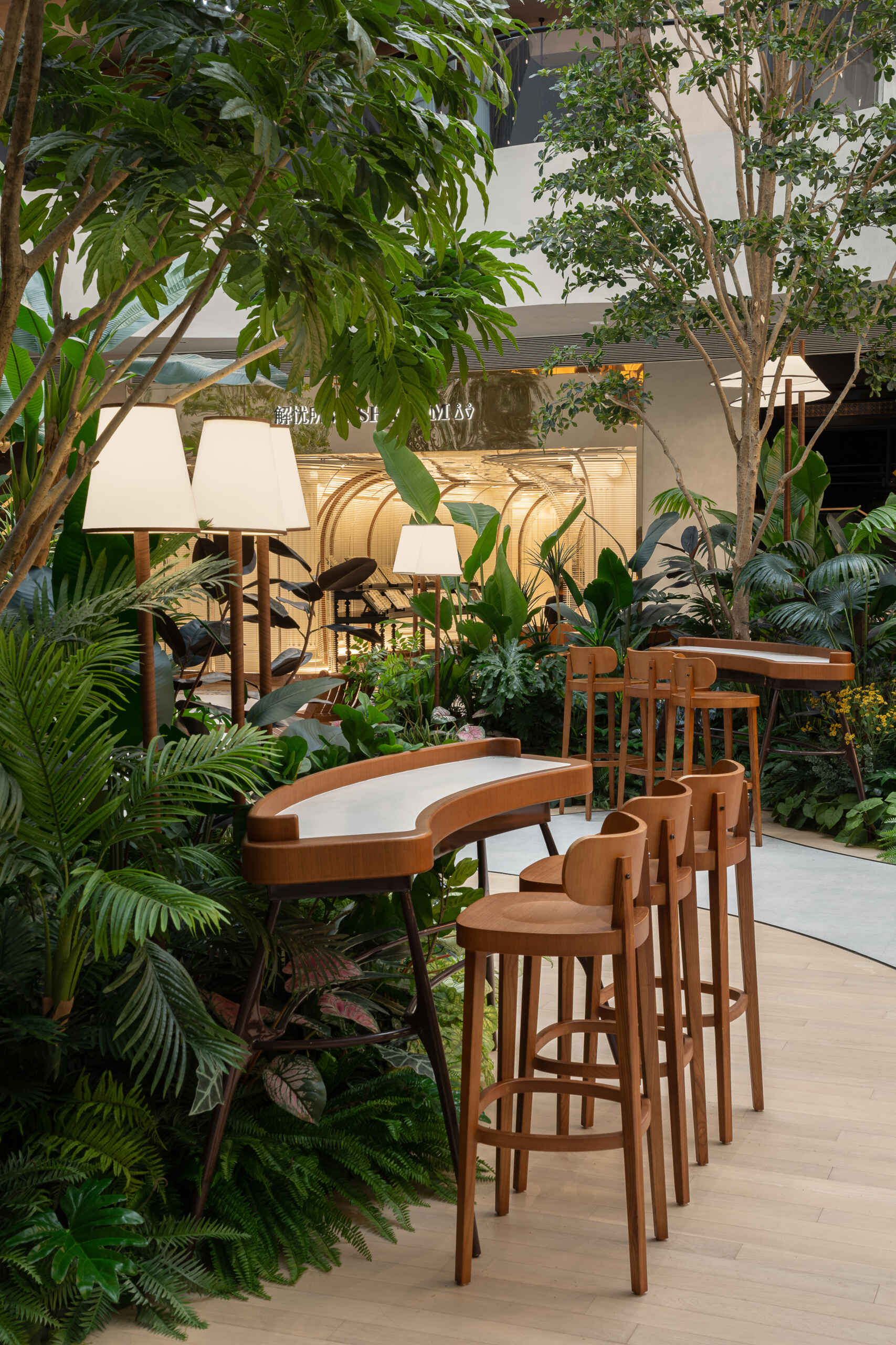 In this public plaza, long benches curve around clusters of greenery while sculptural chairs create relaxed, flexible seating. This dining space flows into a shared public garden, dissolving the line between restaurant and rest stop.