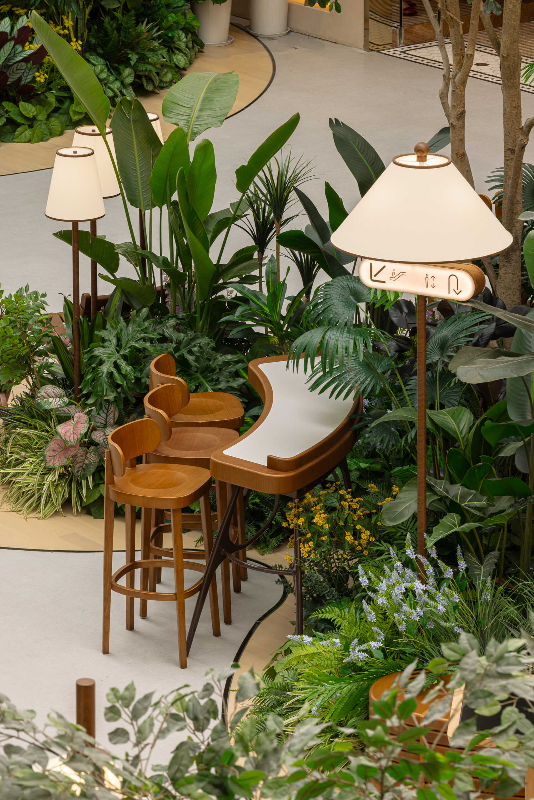 In this public plaza, long benches curve around clusters of greenery while sculptural chairs create relaxed, flexible seating. This dining space flows into a shared public garden, dissolving the line between restaurant and rest stop.