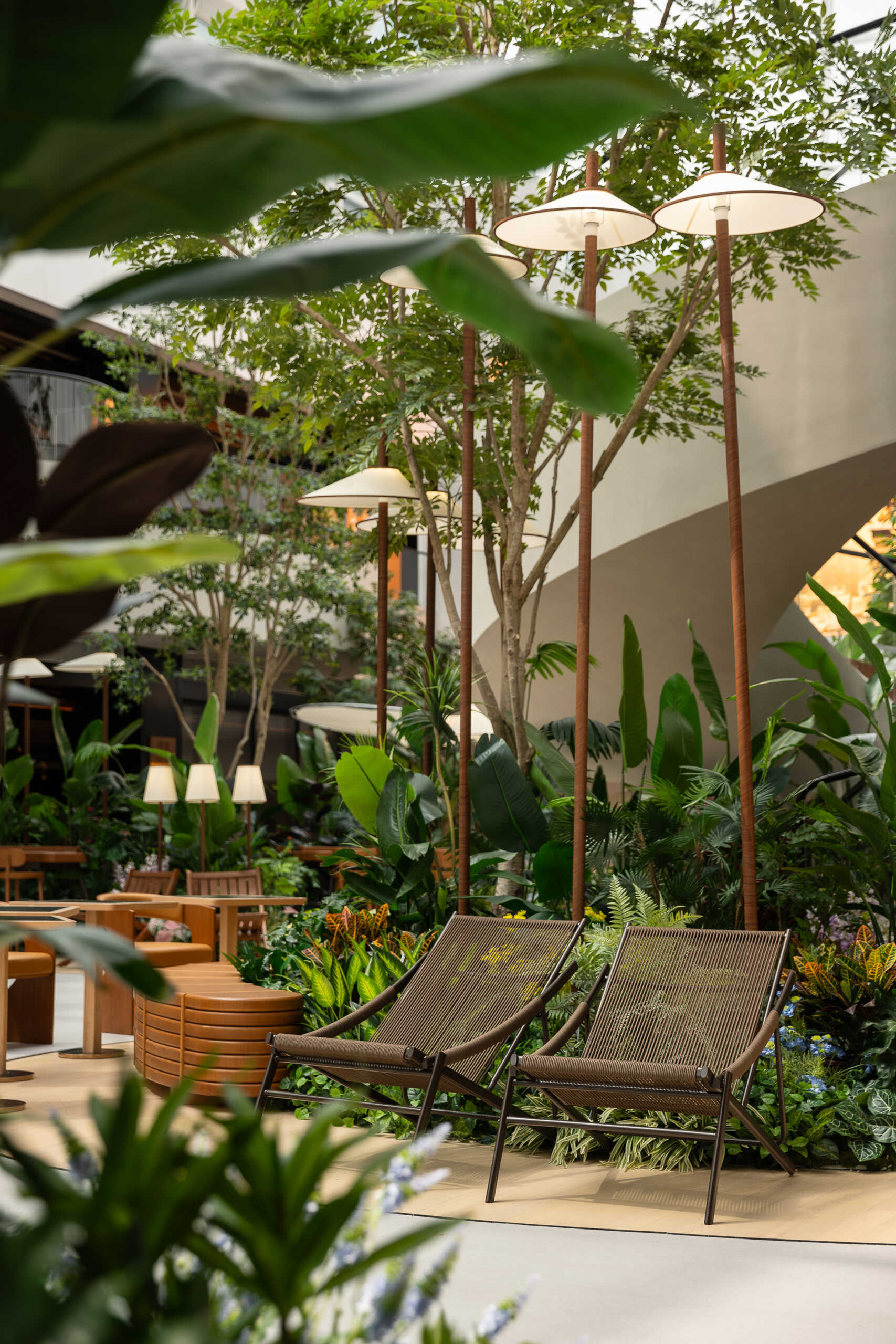 In this public plaza, long benches curve around clusters of greenery while sculptural chairs create relaxed, flexible seating. This dining space flows into a shared public garden, dissolving the line between restaurant and rest stop.