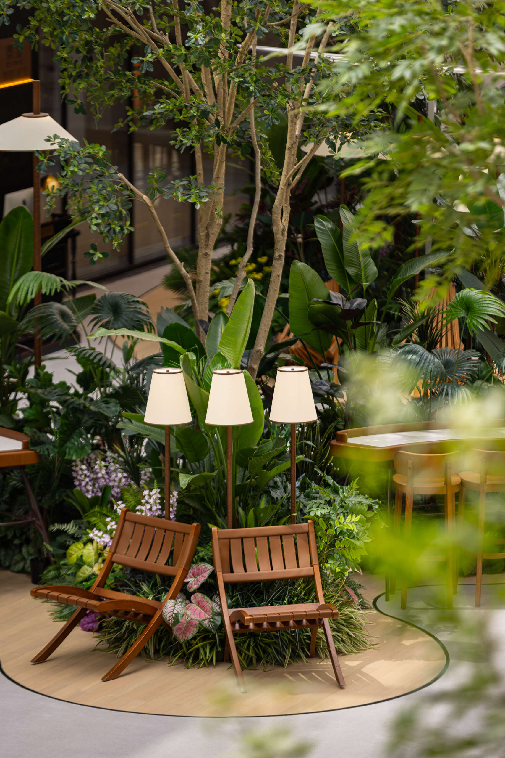 A carefully layered plant palette creates a three-dimensional garden indoors in this plaza. Tall banyans and maples stretch overhead, mid-level jacarandas and palms form soft screens, while low-growing begonias and philodendrons fill the floor. Architecture and greenery move in rhythm, shaping a space that feels alive and intentional.