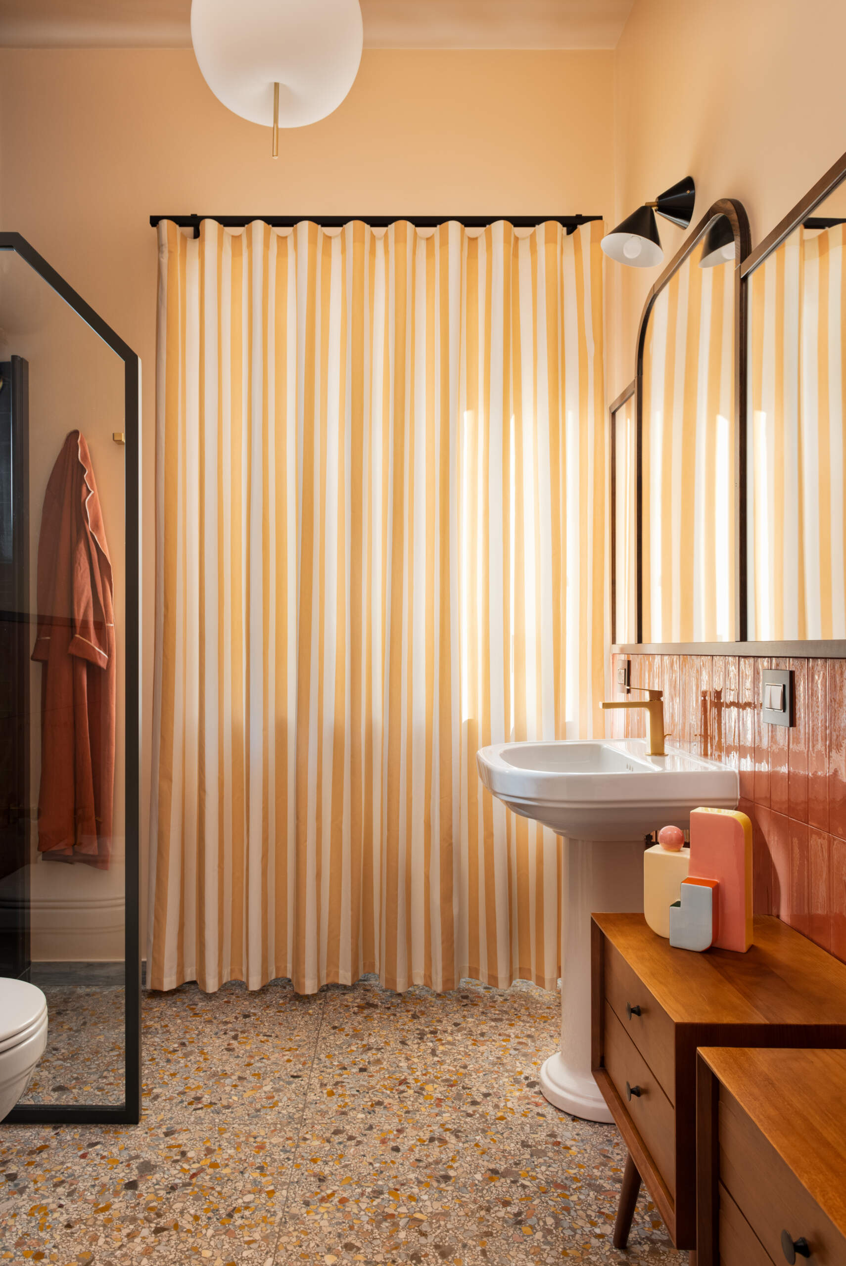 Preceded by a compact laundry zone hidden behind sliding oak wardrobes, this guest bathroom leans into the warmth of its materials. Rust-colored tiles, peach walls, and brass accents evoke a nostalgic nod to the home’s 1960s origin, softened into something cozy and romantic.