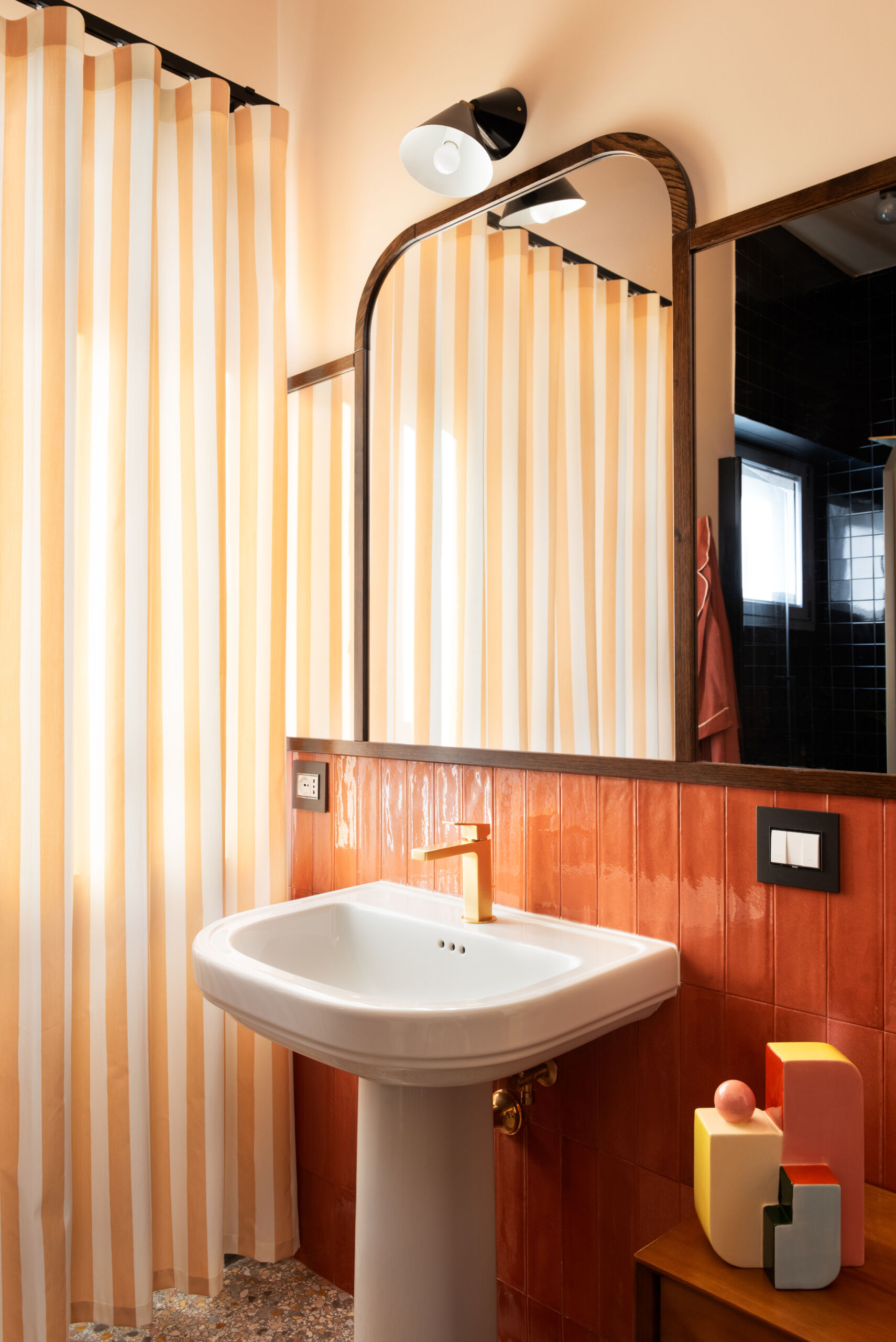 Preceded by a compact laundry zone hidden behind sliding oak wardrobes, this guest bathroom leans into the warmth of its materials. Rust-colored tiles, peach walls, and brass accents evoke a nostalgic nod to the home’s 1960s origin, softened into something cozy and romantic.