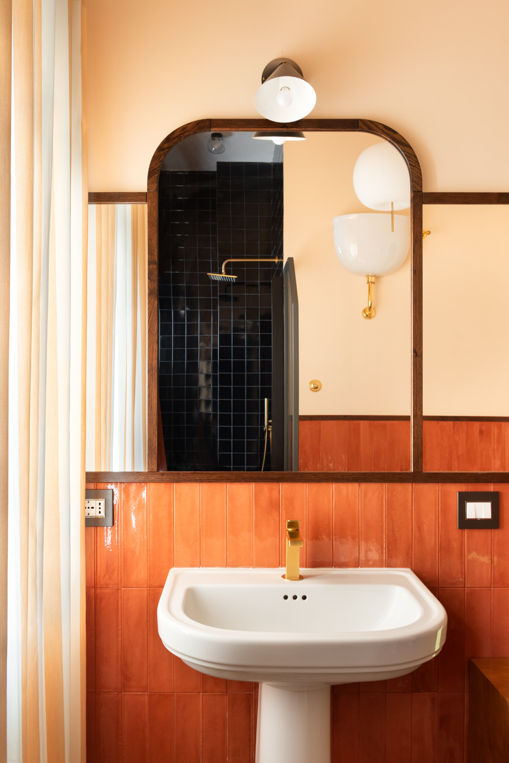 Preceded by a compact laundry zone hidden behind sliding oak wardrobes, this guest bathroom leans into the warmth of its materials. Rust-colored tiles, peach walls, and brass accents evoke a nostalgic nod to the home’s 1960s origin, softened into something cozy and romantic.