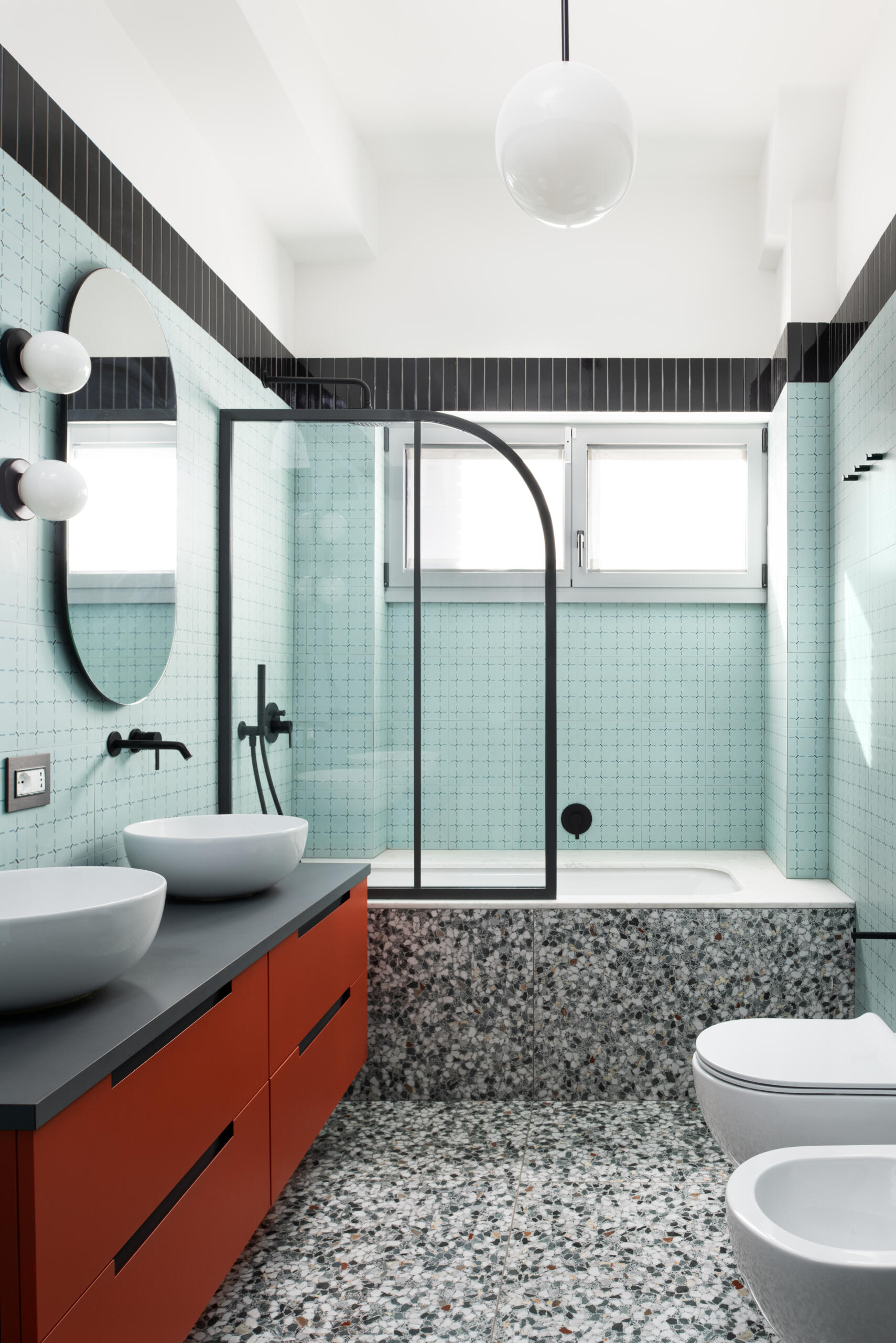 The main bathroom in this renovated 1960s apartment has large format t “Ghiara Minuta Mix” marble-look tiles by Marazzi, while the walls are clad in “Confetti” tiles by Ceramica Vogue in the Torino pattern. Black accents tie all of the design decisions together.