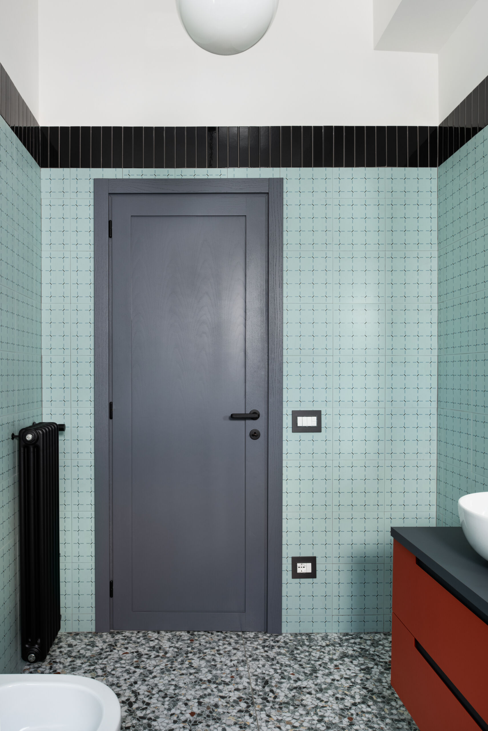 The main bathroom in this renovated 1960s apartment has large format t “Ghiara Minuta Mix” marble-look tiles by Marazzi, while the walls are clad in “Confetti” tiles by Ceramica Vogue in the Torino pattern. Black accents tie all of the design decisions together.