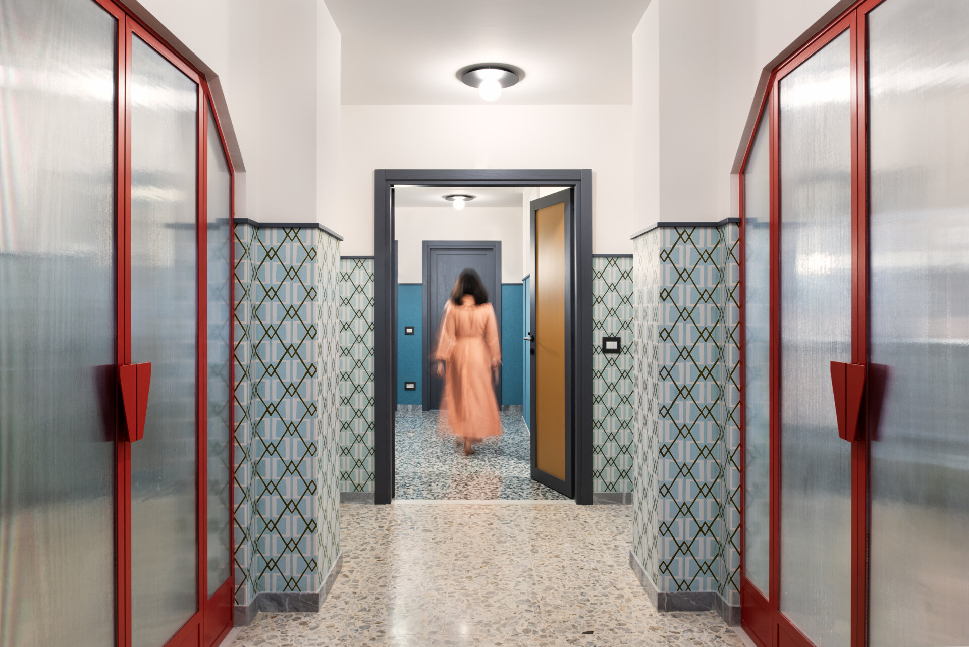 In this renovated 1960s apartment, the entryway pairs bold boiserie with lacquer-red glass doors that visually anchor the space.