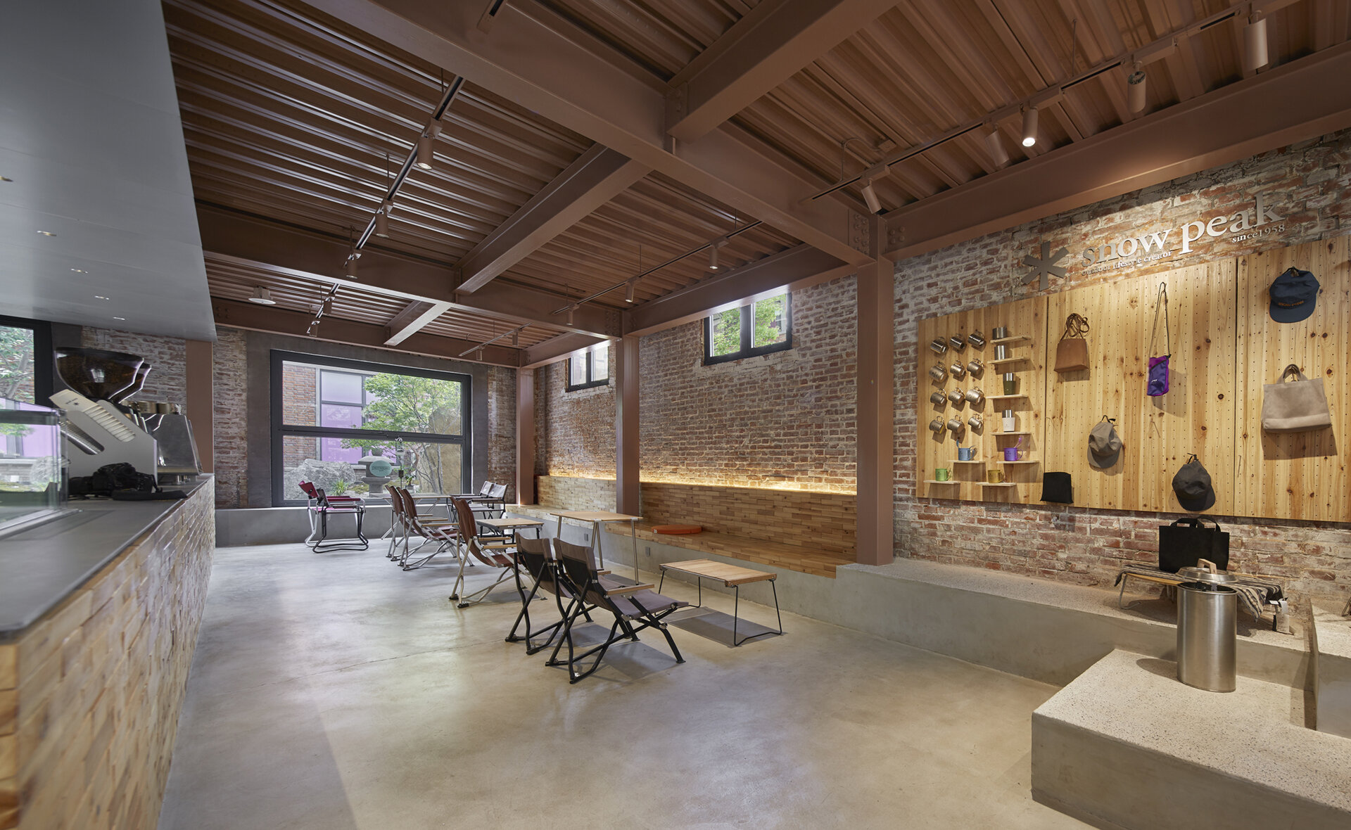 Brown-painted steel columns, beams, and ceiling harmonize with the warm tones of this renovated red-brick warehouse cafe, resembling wood at first glance. Built-in benches with hidden lighting define the seating areas.