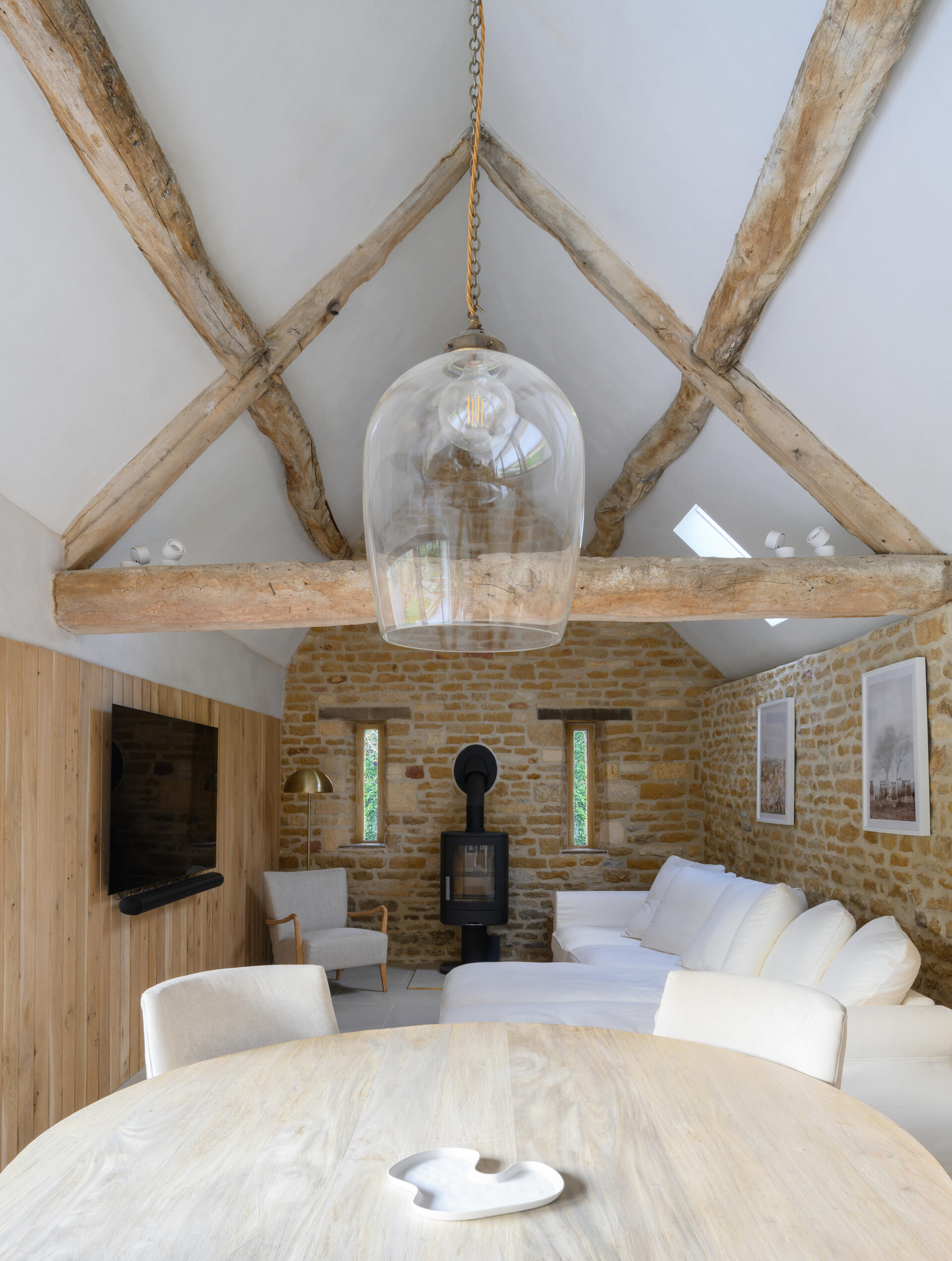 The main living space of this renovated cowshed is understated and relaxed, with a focus on texture rather than decoration. Exposed timber beams run across the living area, adding depth and authenticity to the otherwise minimal interior. Their weathered texture contrasts gently with the raw lime plaster and clean lines of the new insertions. Rather than conceal or restore them too much, the beams were left largely untouched, allowing the marks of time to remain visible and grounding the space in its agricultural past.