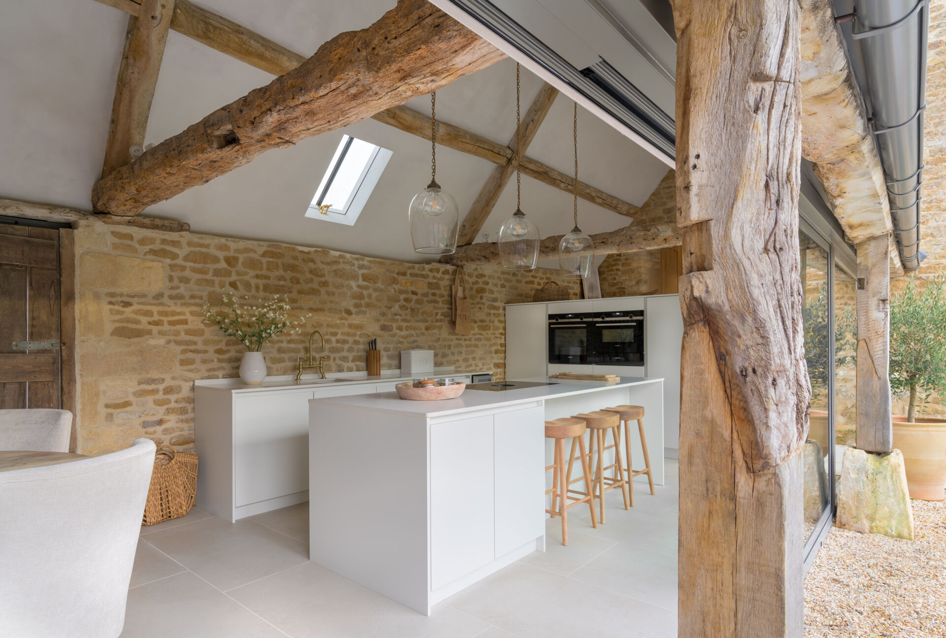 In this renovated cowshed, the dining area separates the living room and kitchen, which is designed to feel both functional and unfussy. Materials were kept simple and durable, aligning with the overall aesthetic. Timber detailing continues here, reinforcing the warm tones that run throughout the home. The layout allows for social cooking, without drawing attention away from the structure itself.