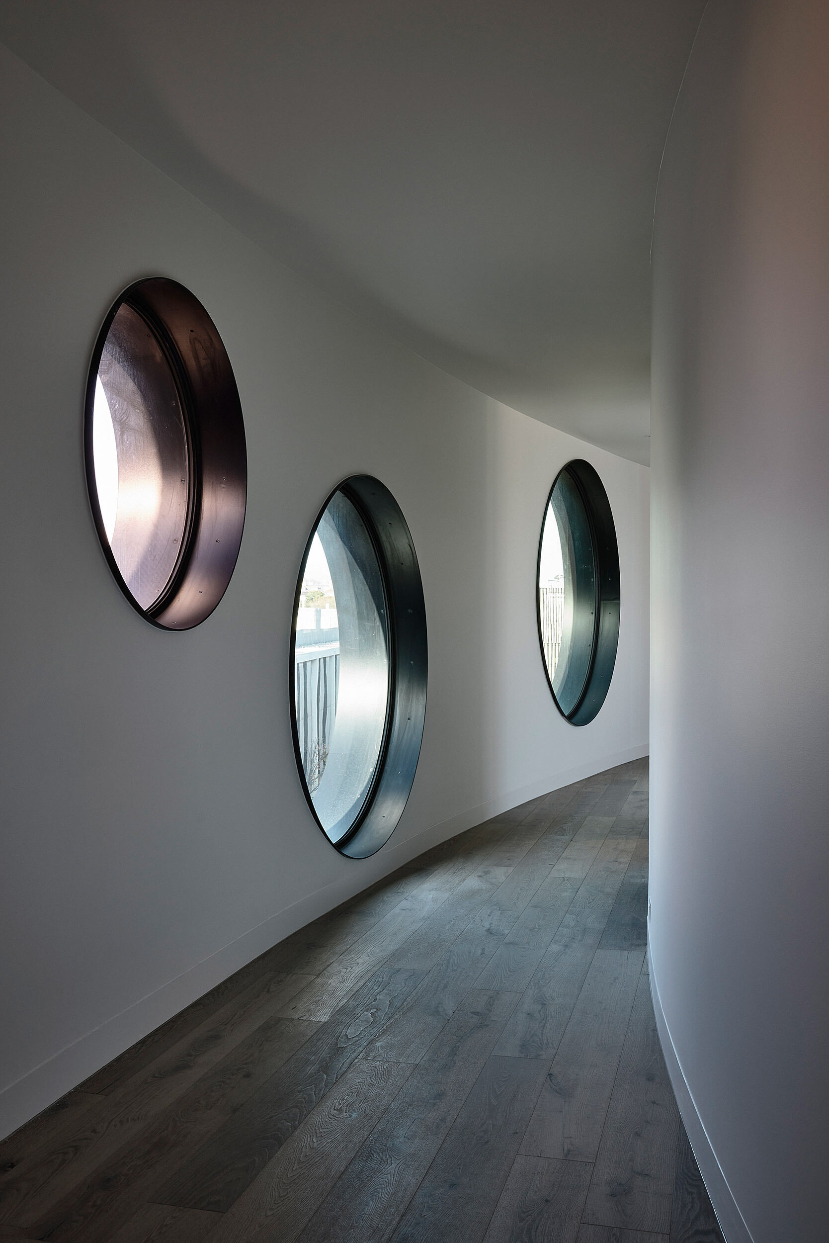 A standout detail is the use of round windows in the apartment facade, a subtle nod to coastal architecture that adds softness and a sense of play to the otherwise sculptural forms. They frame views like portholes, reinforcing the project’s connection to the bay just beyond.