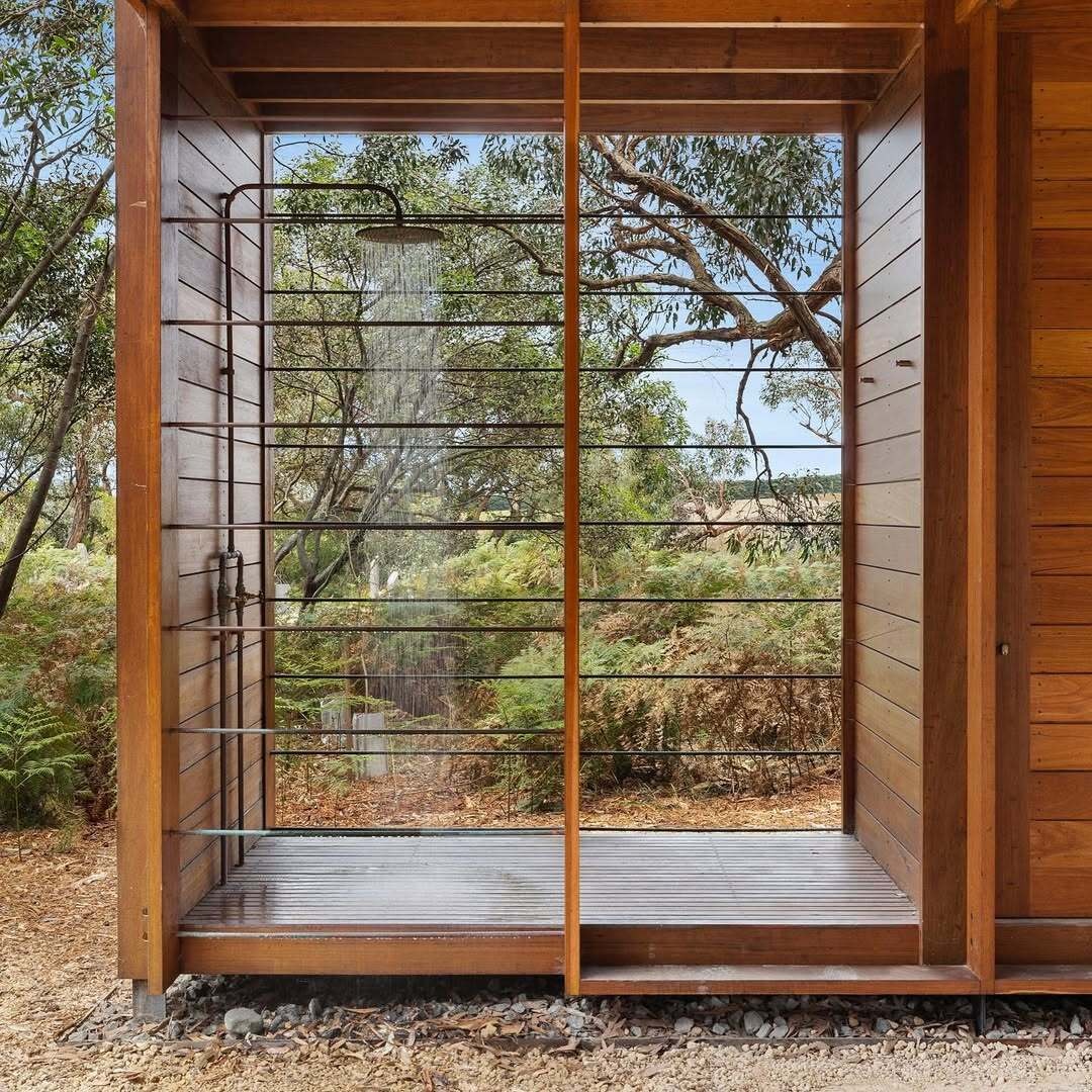 An outdoor shower positioned near the carport and designed for barefoot returns from the beach. It invites residents to rinse off under open sky before re-entering the home.