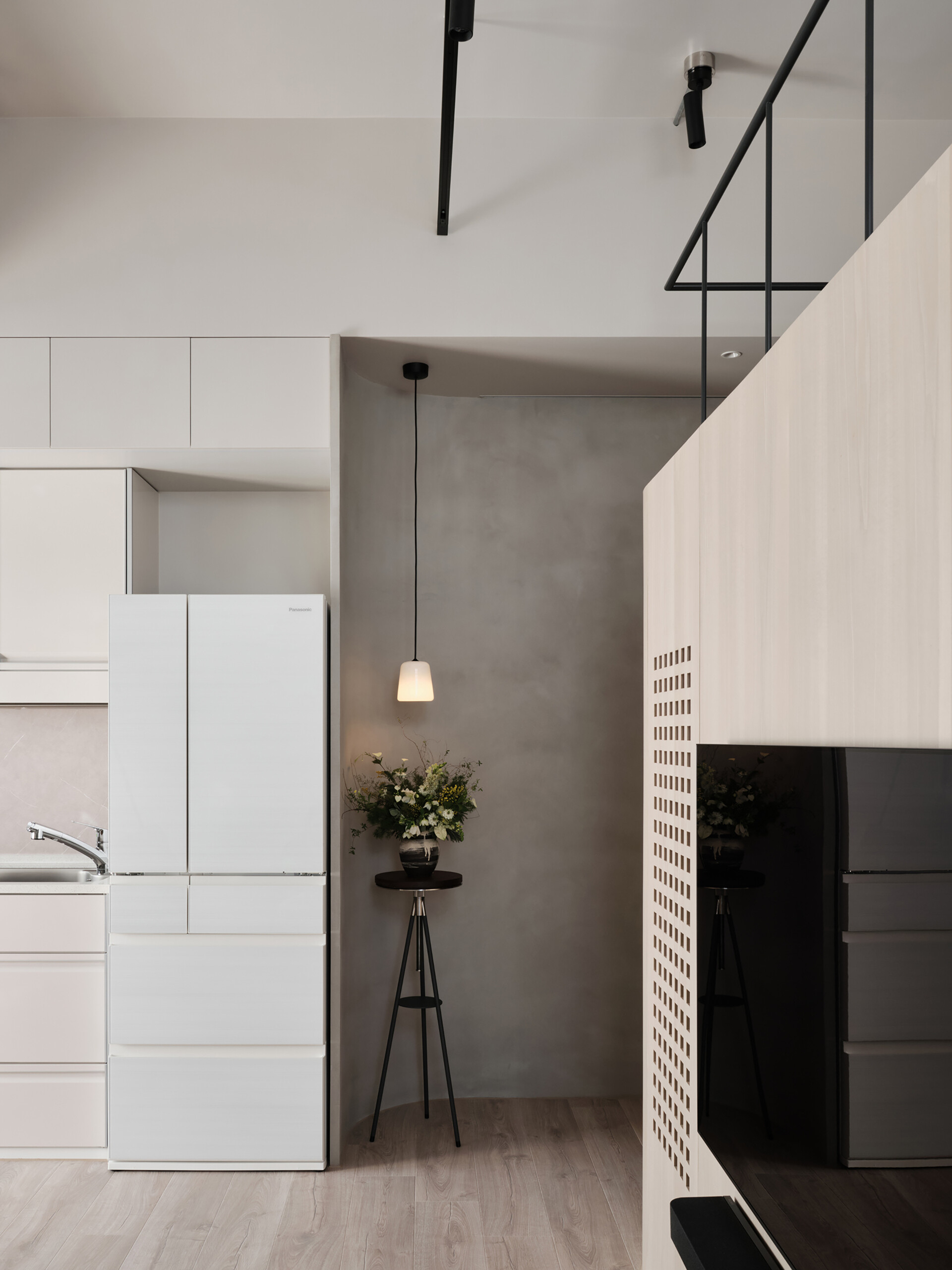This compact kitchen feels effortlessly refined, with sleek cabinetry in a soft, warm beige that blends seamlessly into the walls. A subtle stone-look backsplash and pale wood flooring keep the palette light and harmonious. Built-in appliances, including a cooktop and washing machine, are tucked neatly into the lower cabinets, maximizing functionality without disrupting the flow.